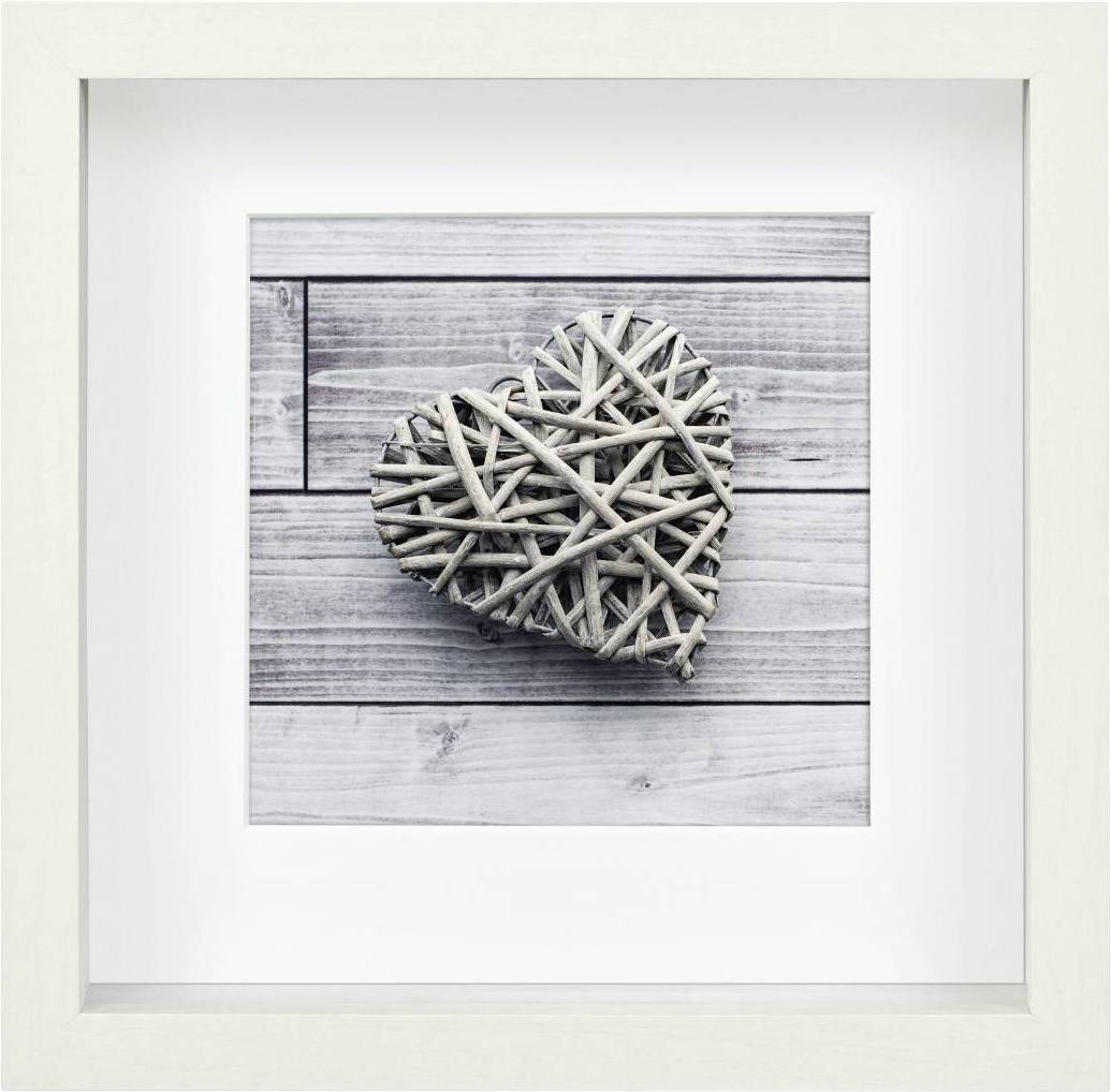 Ein Herz aus verflochtenen Zweigen liegt auf einem Holzhintergrund. Einfache, natürliche Dekoration in einem weißen Rahmen.