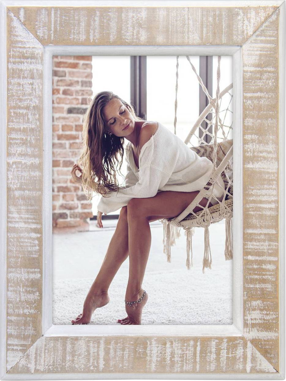 Eine Frau sitzt in einem Hängesessel vor einem Backsteinfenster, sie trägt einen weißen Pullover und lächelt entspannt.