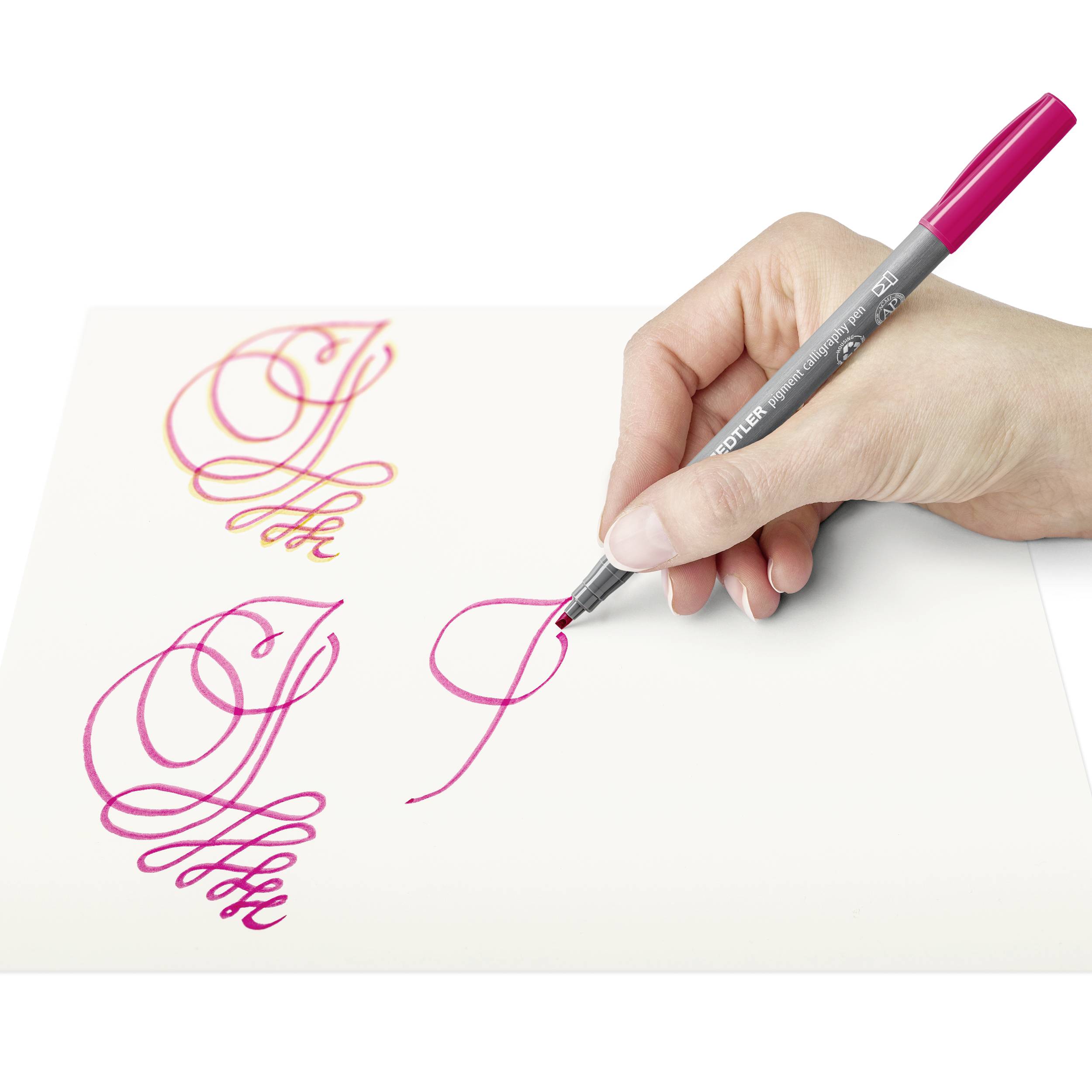 Eine Hand schreibt mit einem pinken Stift kalligrafische Buchstaben auf weißem Papier.