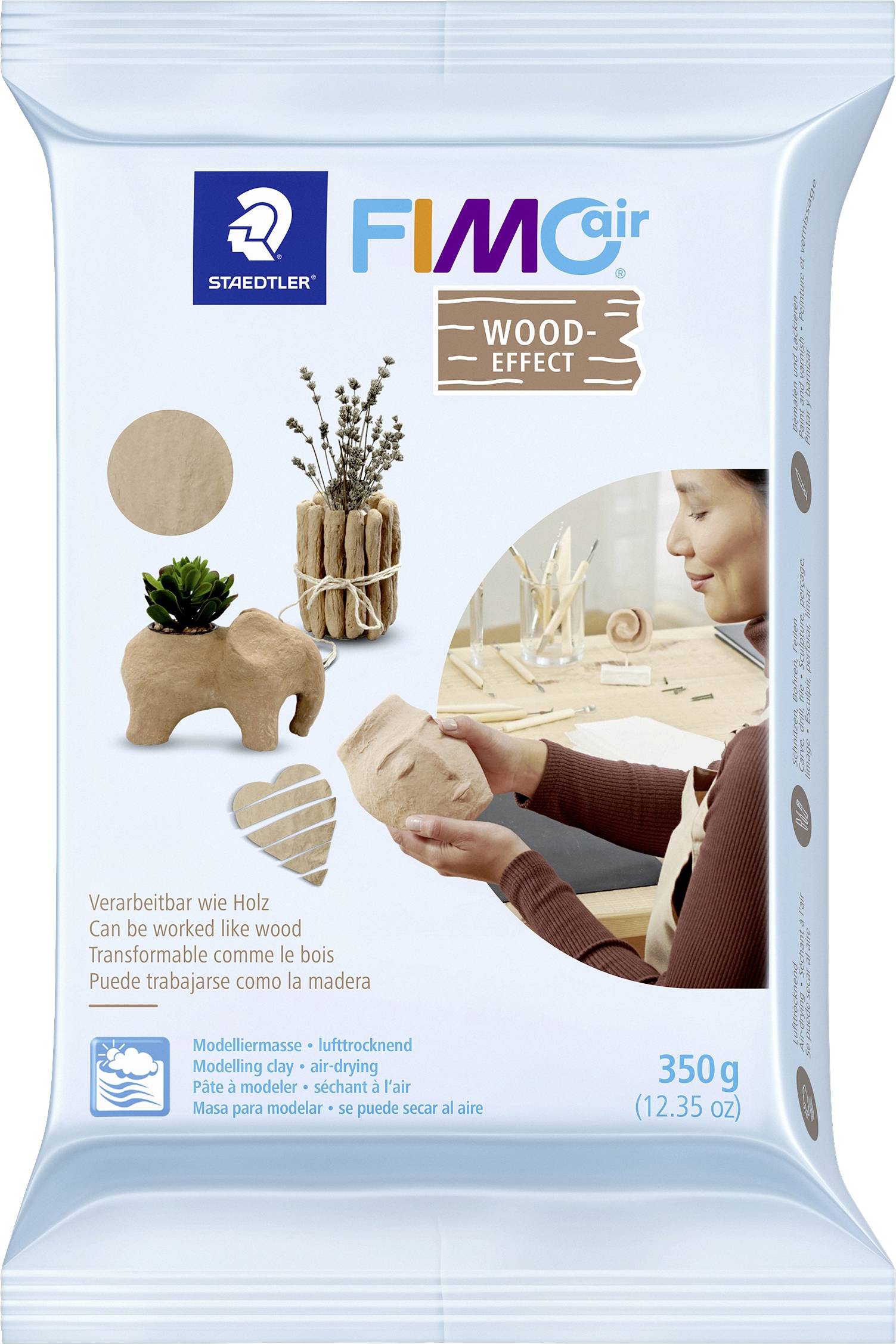 Verpackung von FIMOair Wood-Effekt, 350g. Zeigt Modelliermasse und fertige Modelle: Elefant, Herz, Bastelaccessoires. 'Verarbeitbar wie Holz'.
