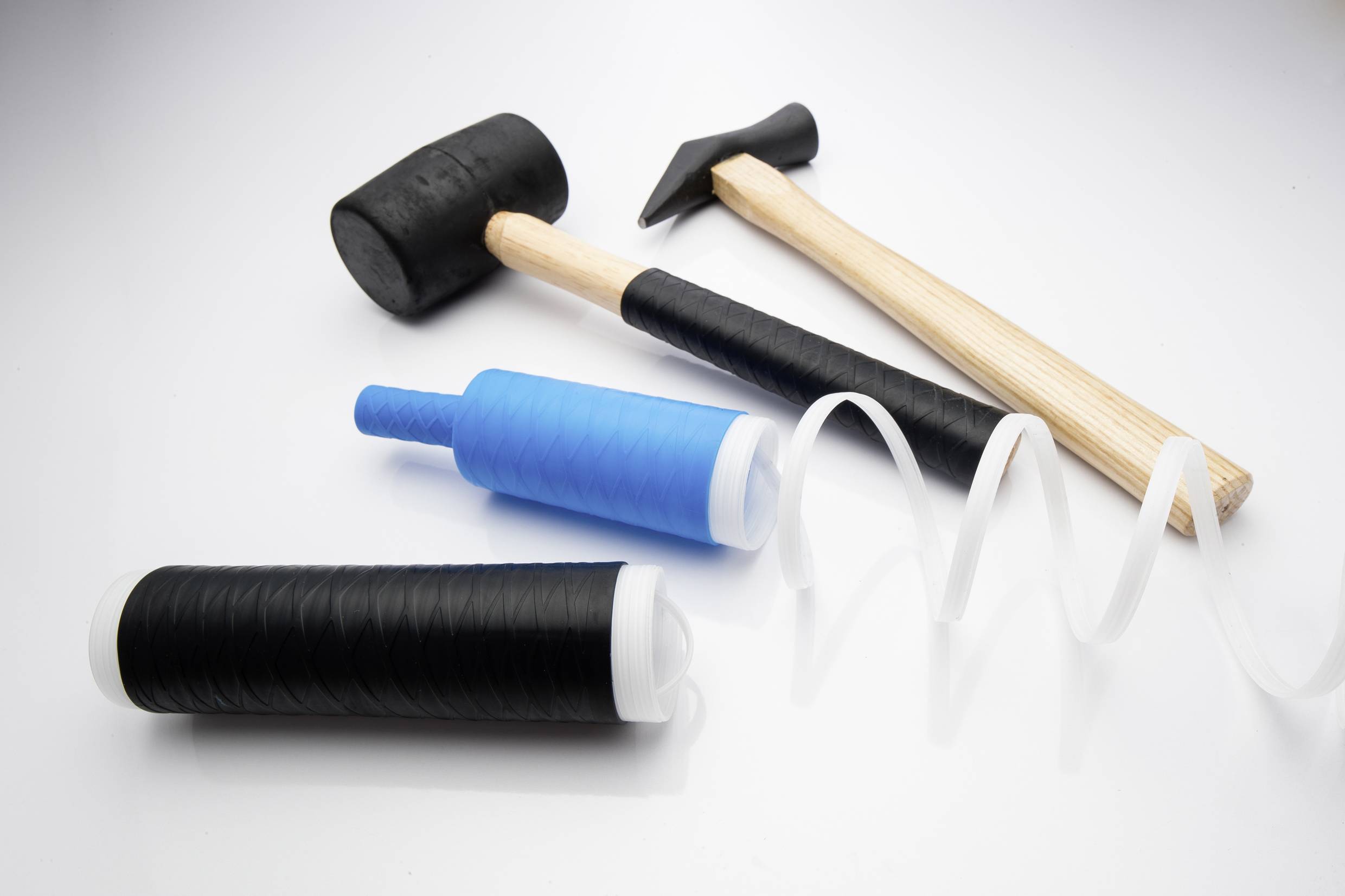 Zwei Hämmer aus Gummi und Holz, zwei schwarze und eine blaue Dehnfolie auf Rollen, auf weißem Hintergrund arrangiert.