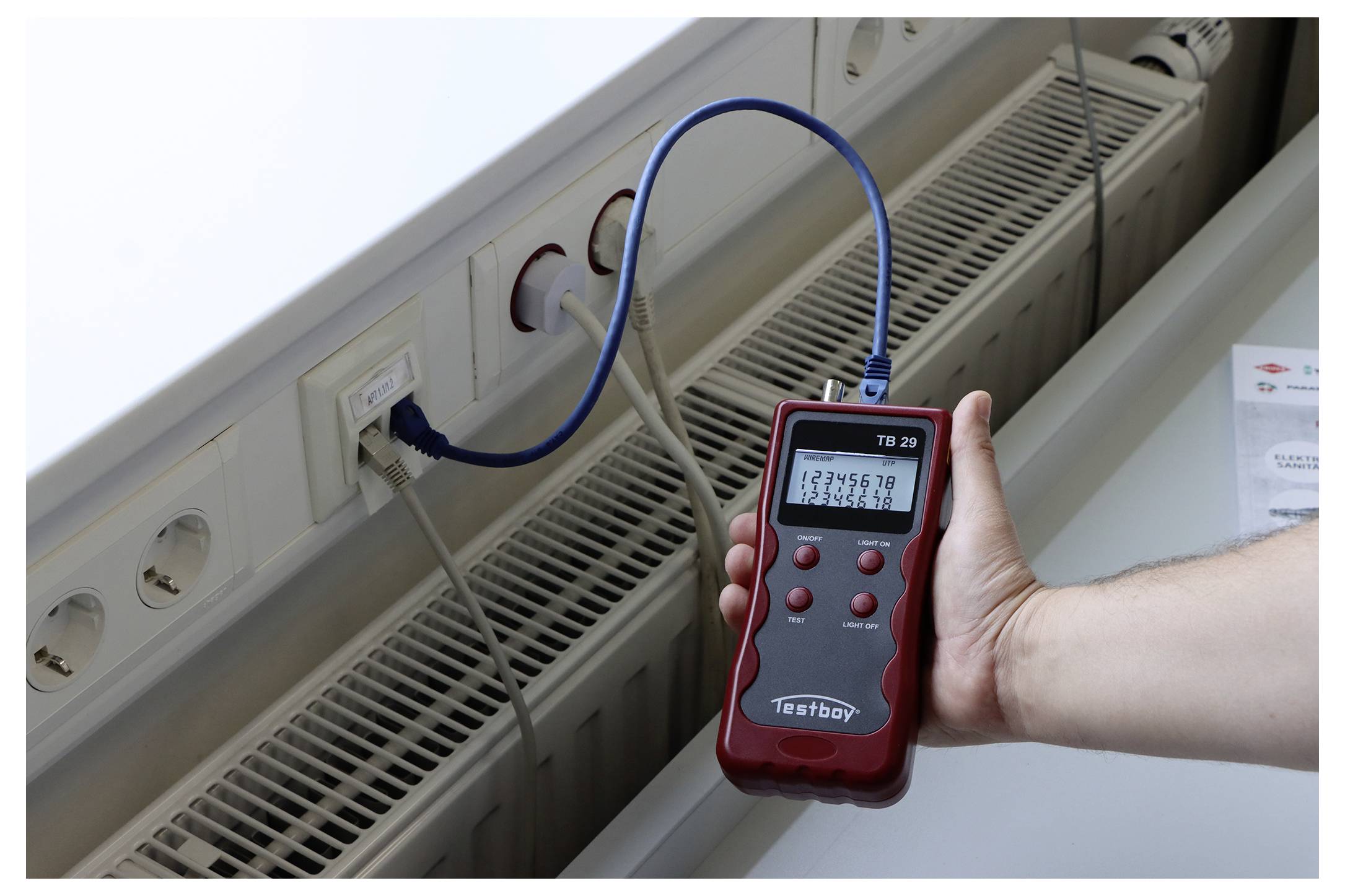 Eine Hand hält einen roten Netzwerktester, der Zahlen anzeigt, verbunden mit einem Netzwerkport durch ein blaues Kabel, das einen laufenden Test anzeigt.