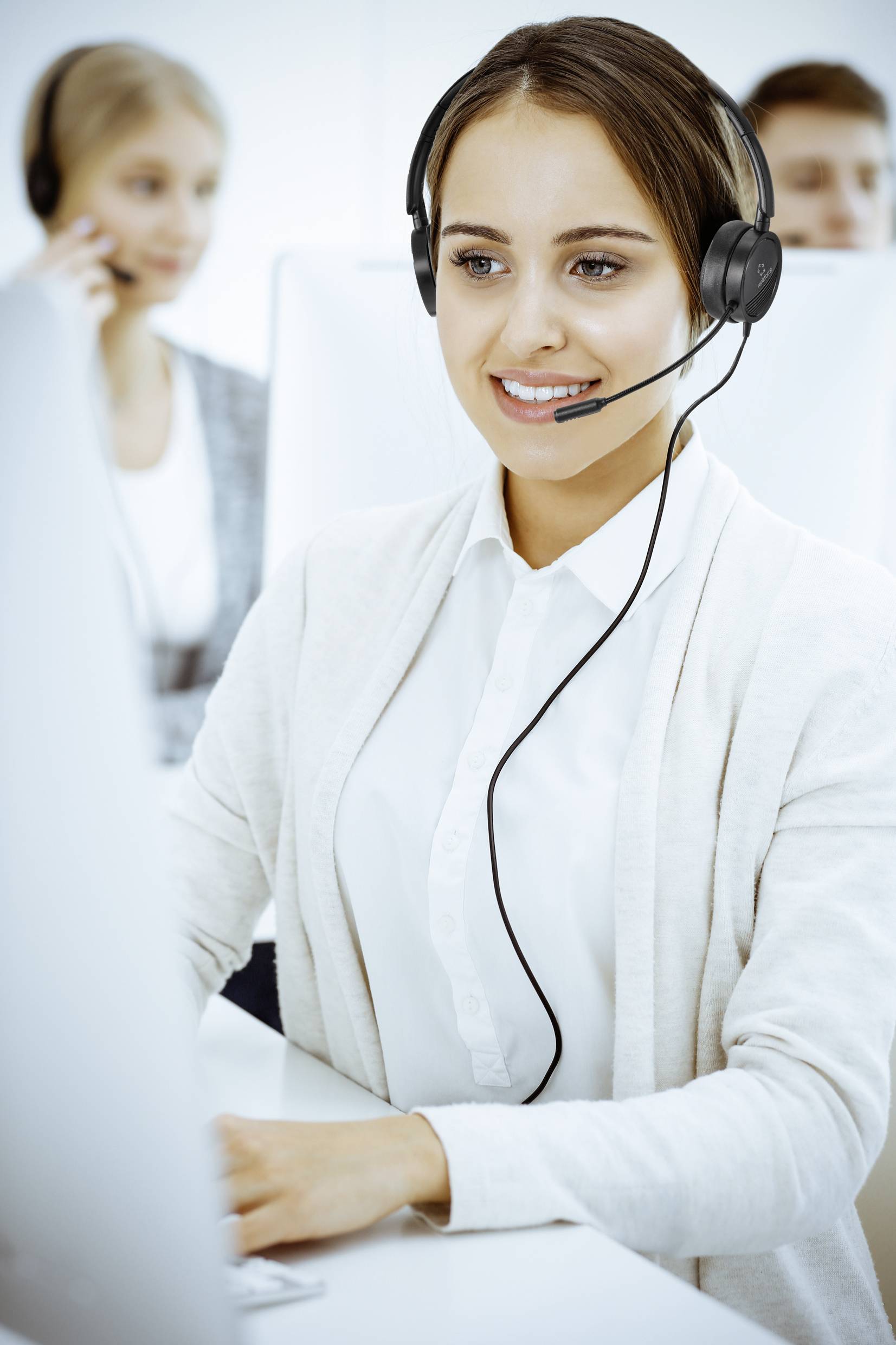 Frau mit Headset arbeitet an einem Computer in einem Büro, während andere Mitarbeiter im Hintergrund ebenfalls telefonieren.
