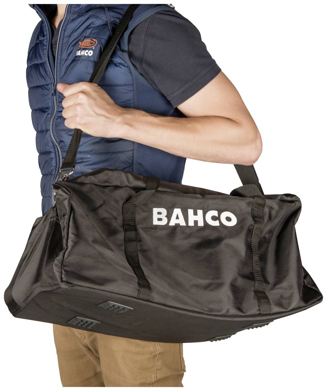 Person trägt eine schwarze BAUCO-Tasche über der Schulter. Die Tasche hat einen großen, weißen Schriftzug 