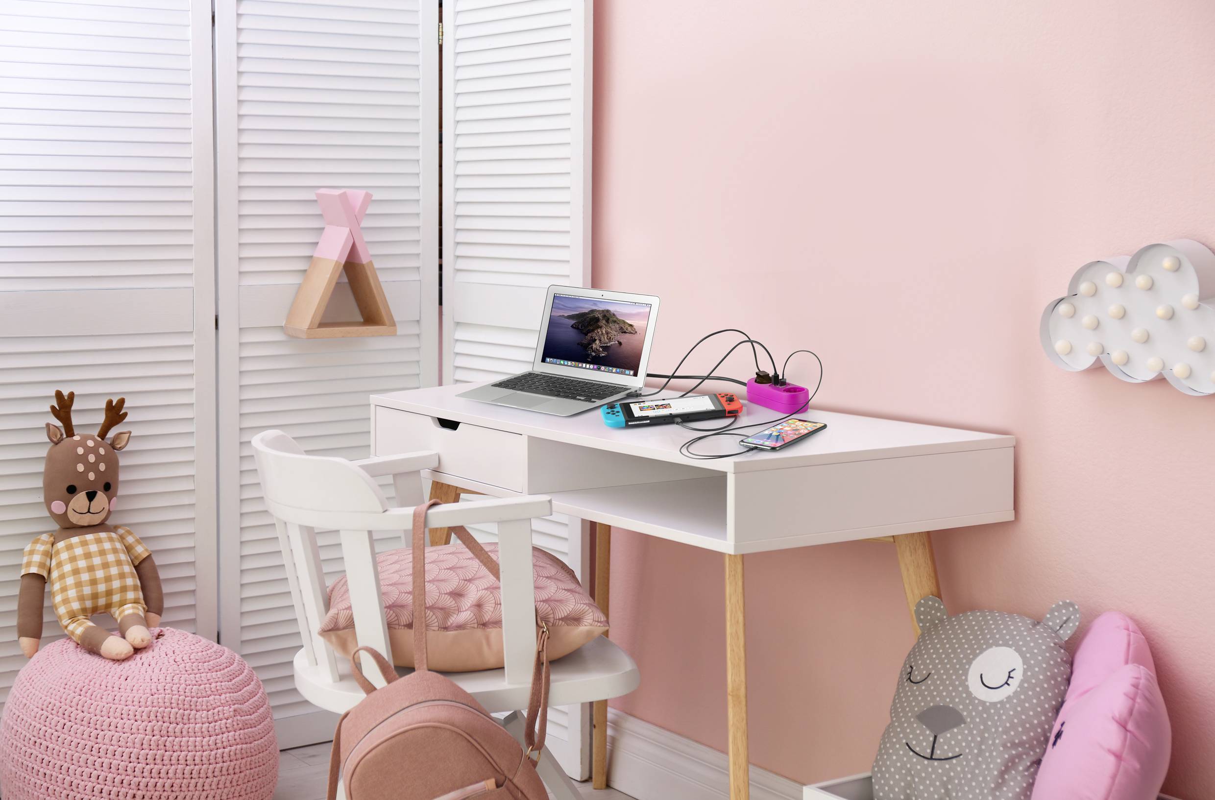 Ein Kinderzimmer mit einem Schreibtisch, Laptop, Notizbuch und Stiften. Rosa Wände und Dekorationen, inkl. Kuscheltier und Kissen.