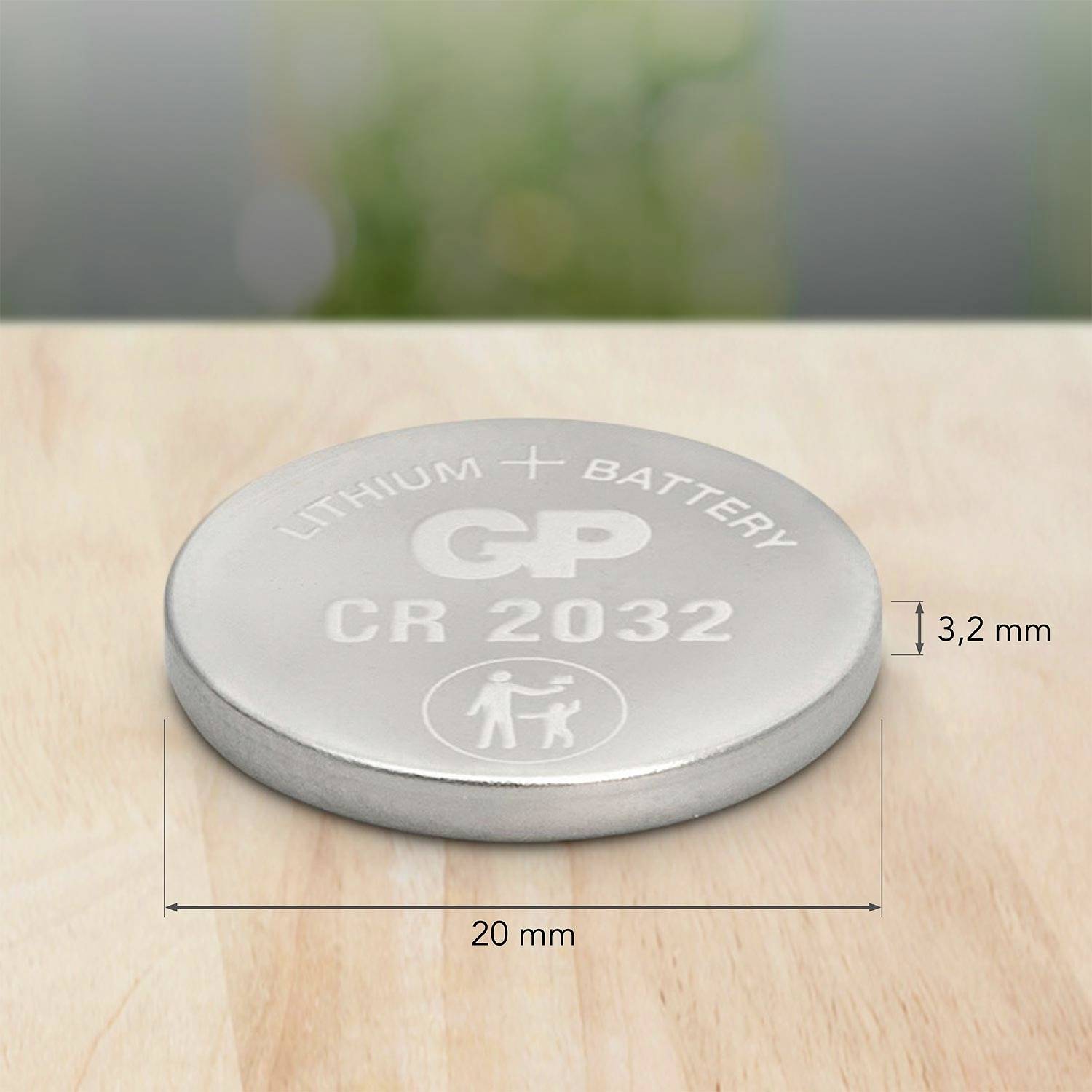Silberne Knopfzellenbatterie der Größe CR2032 auf Holztisch, mit Aufschrift 'LITHIUM BATTERY GP CR 2032', Durchmesser 20 mm.