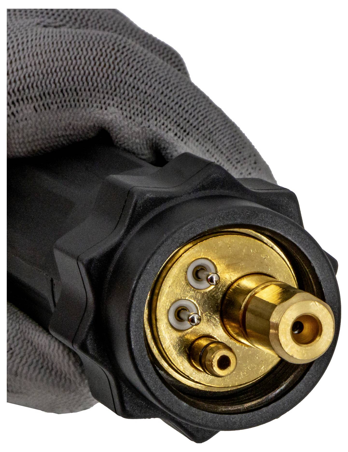 Nahaufnahme einer behandschuhten Hand, die einen schwarzen Stecker mit einer goldenen Kreisfläche und drei Metallkontaktstiften hält.