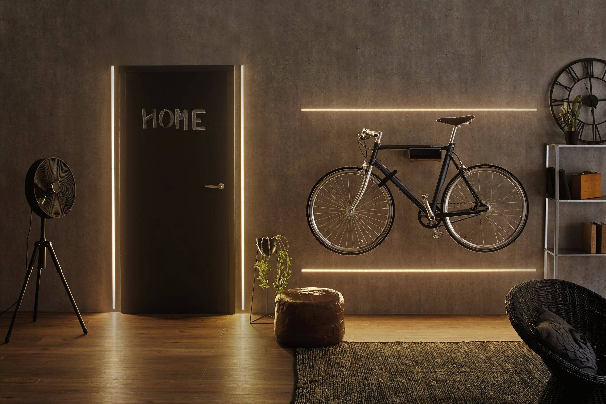 Ein stilvolles Wohnzimmer mit einem an der Wand montierten Fahrrad, links eine Tür mit 'HOME' und rechts ein Bücherregal.