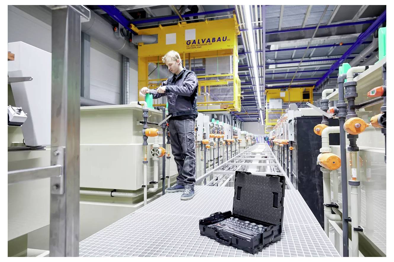 Ein Techniker in einer Werkstatt bedient Maschinen auf einem Industrie-Laufweg, mit Ausrüstung und Werkzeugen im Vordergrund, die eine geschäftige Arbeitsumgebung schaffen.