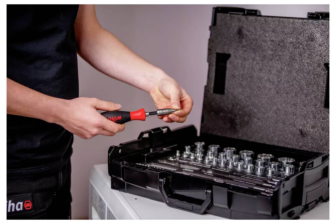 Eine Person stellt ein Werkzeug aus einem Werkzeugsatzes ein, der verschiedene Steckkomponenten in einem schwarzen Koffer enthält, möglicherweise für mechanische Arbeiten.