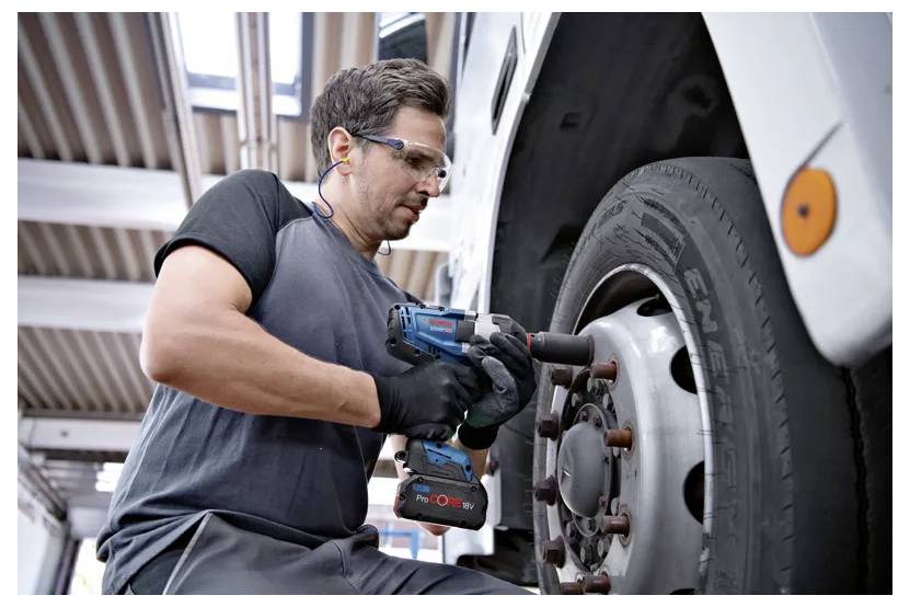 Mechaniker, der einen kabellosen Schlagschrauber verwendet, um eine Radmutter eines Busrads in einer Werkstatt anzuziehen.