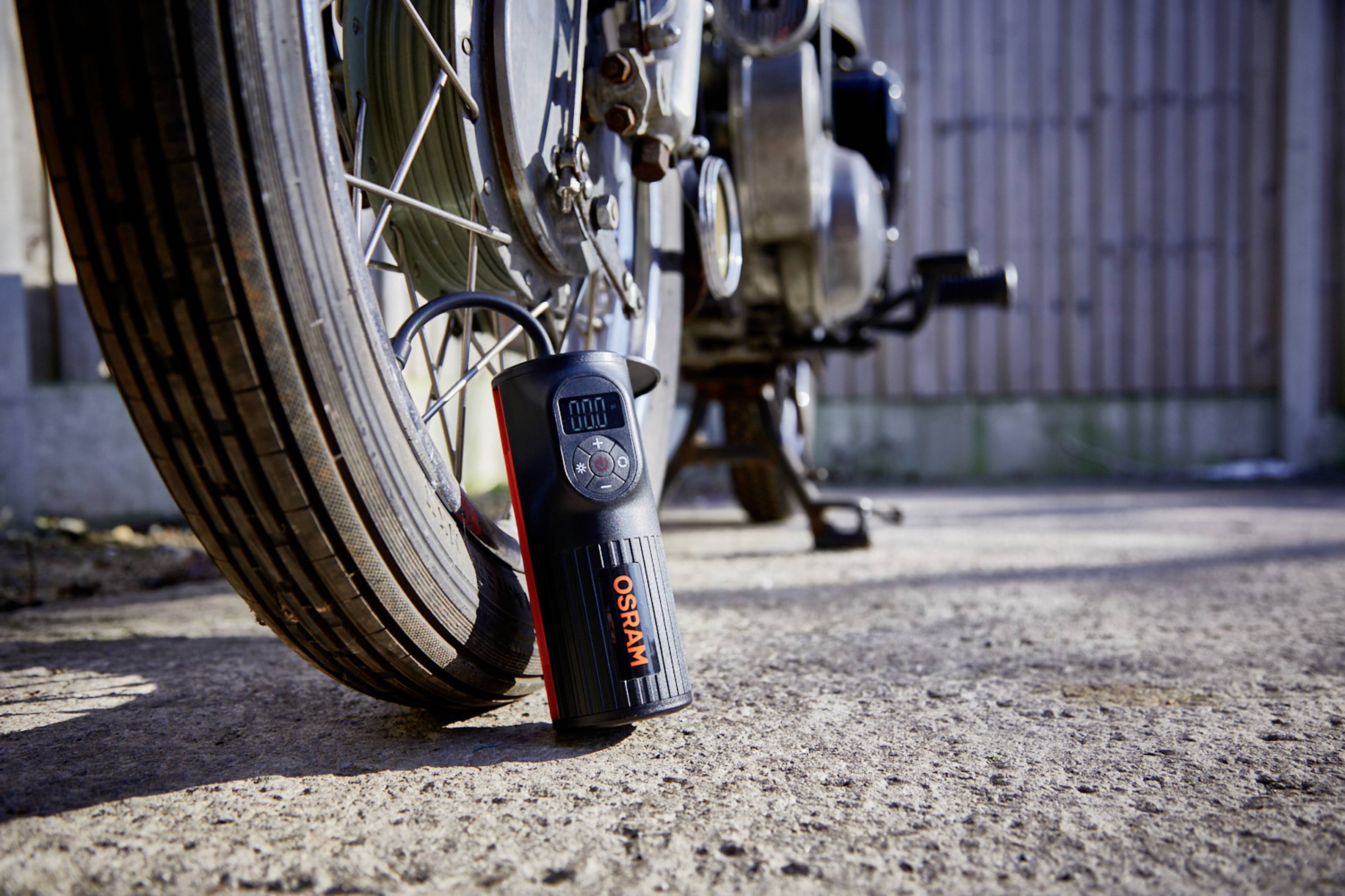 Ein digitales Reifendruckmessgerät liegt auf dem Boden neben einem Motorradreifen und zeigt den Luftdruck an.