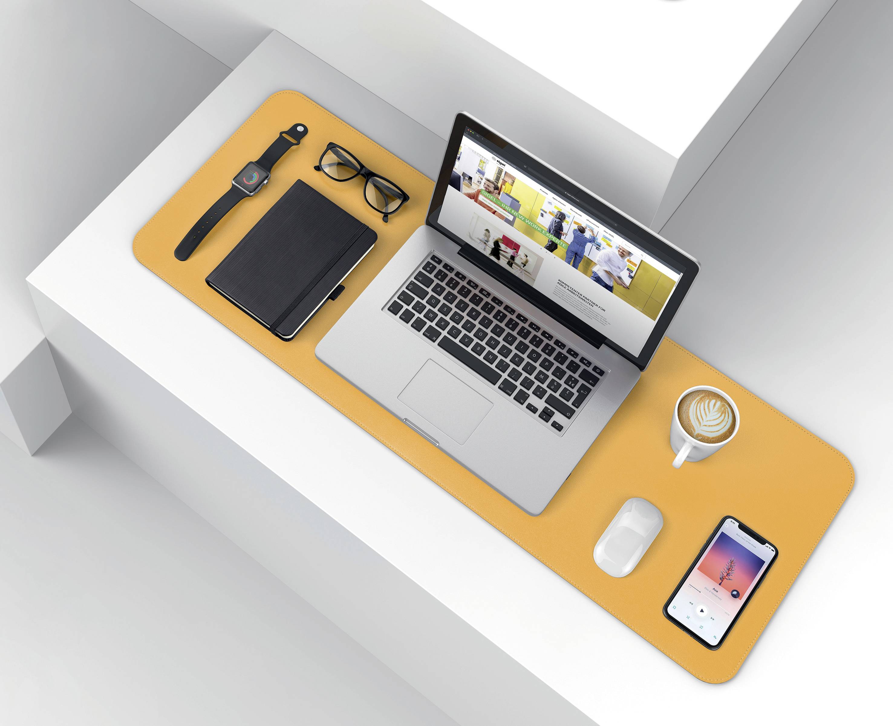 Ein Laptop mit geöffneter Webseite, eine Tasse Cappuccino, eine Smartwatch, eine Brille, ein Notizbuch und ein Smartphone auf einem Tisch.
