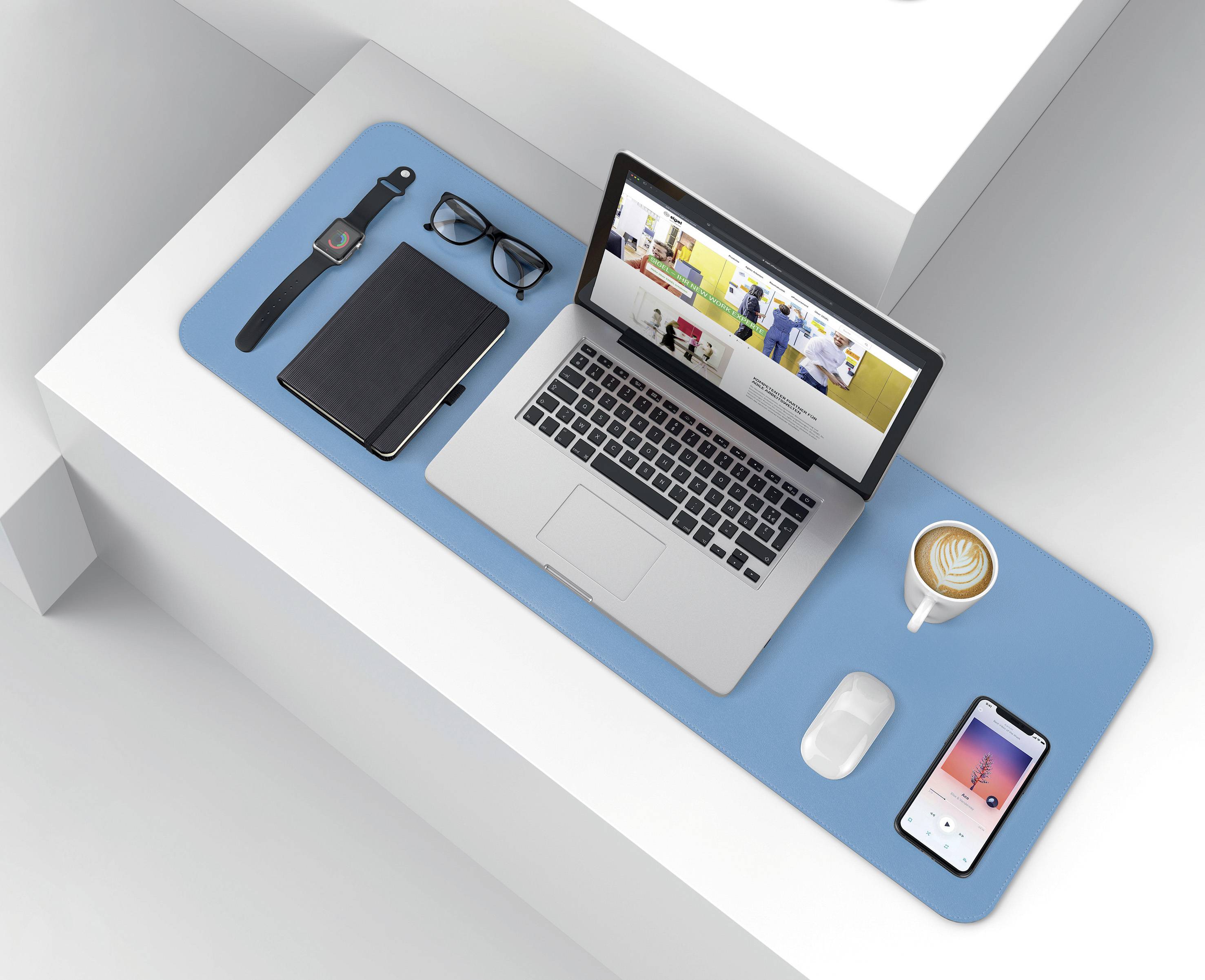 Ein ordentlich organisierter Schreibtisch mit Laptop, Handy, Notizbuch, Brille, Uhr und einer Tasse Cappuccino auf blauer Unterlage.