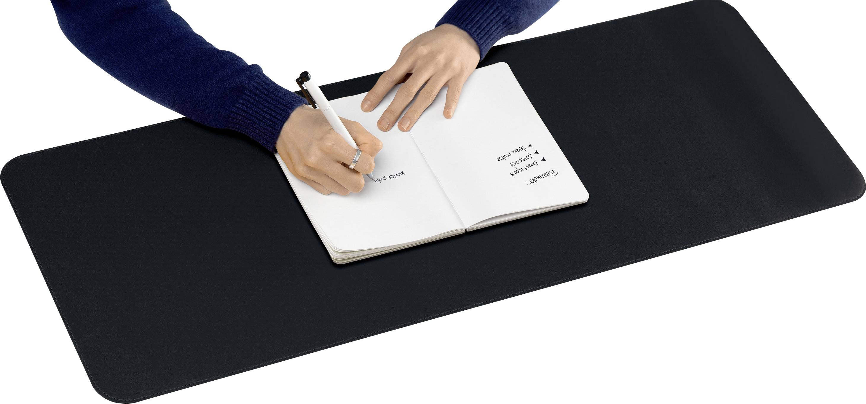 Eine Person schreibt mit einem Stift in ein aufgeschlagenes Notizbuch auf einem schwarzen Schreibtischunterlage.
