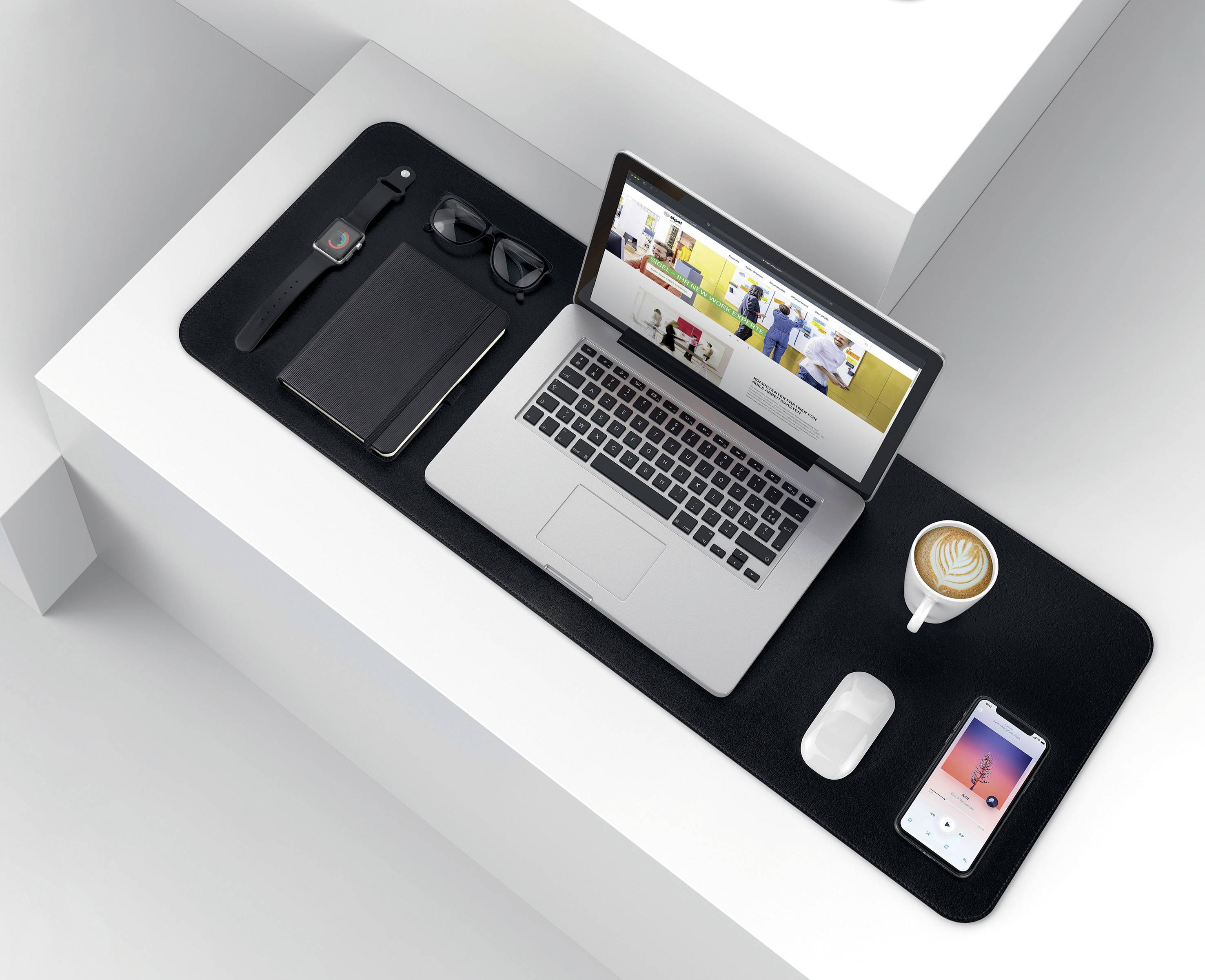 Ein ordentlich angeordneter Schreibtisch mit Laptop, Kaffeetasse, Smartphone, Notizbuch, Kopfhörern und einer Smartwatch.