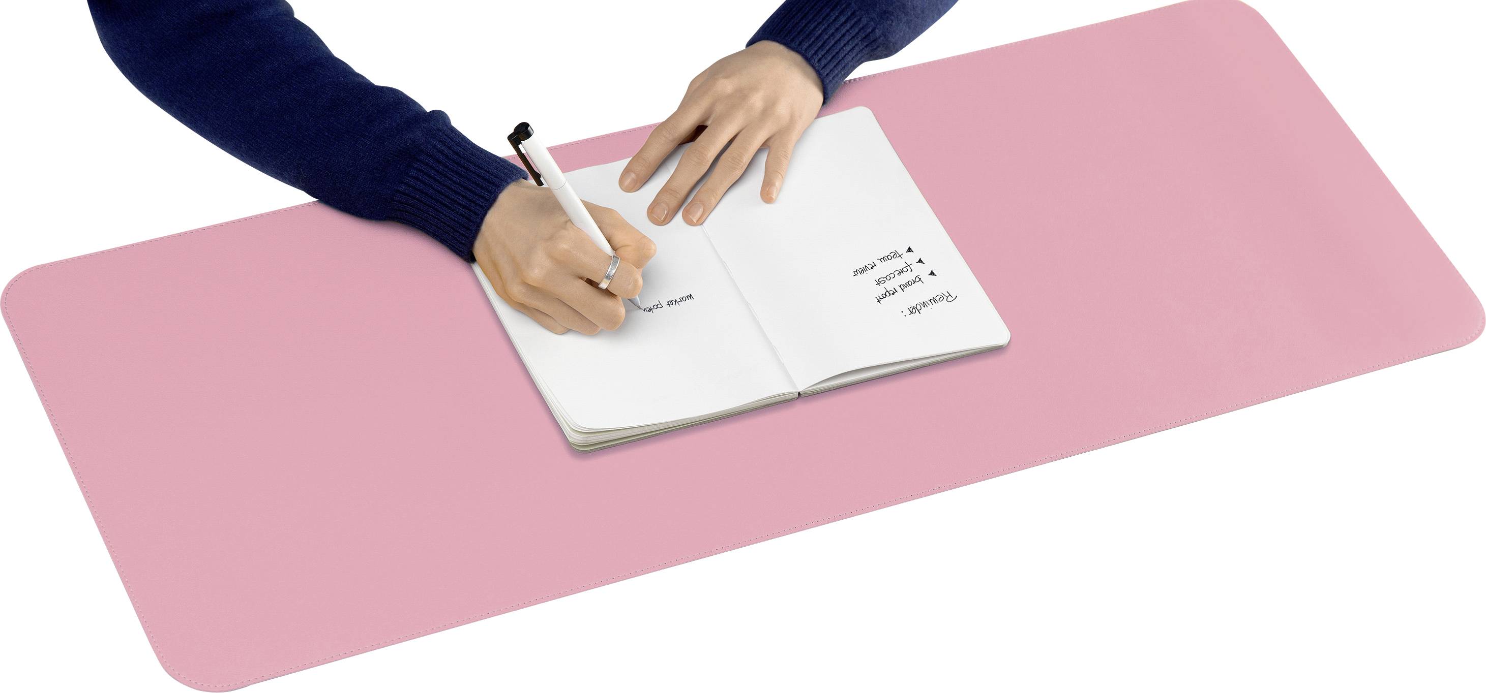 Eine Person schreibt mit einem Stift in ein Notizbuch auf einem großen pinken Schreibtischunterlage.