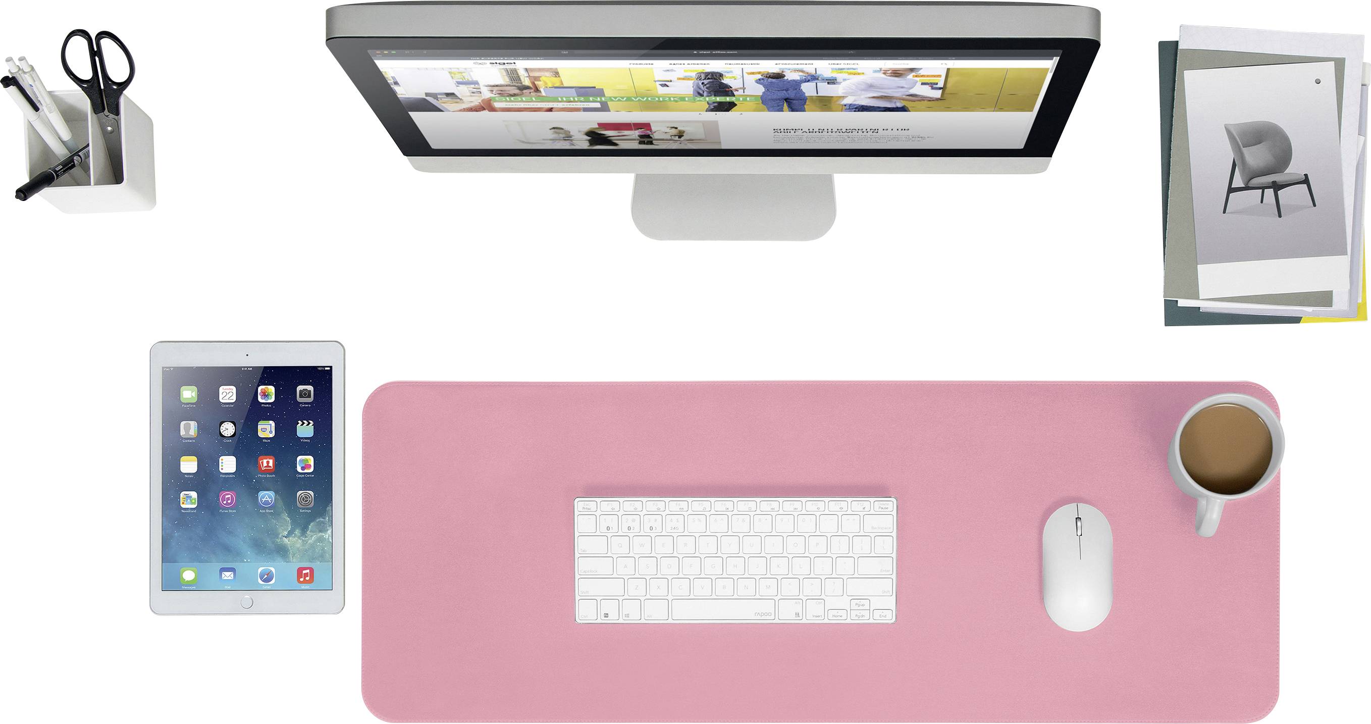 Ein Schreibtisch mit Monitor, Tastatur und Maus auf einer rosa Matte, daneben ein Tablet, Stiftehalter und eine Tasse Kaffee. Im Hintergrund liegen einige Broschüren.