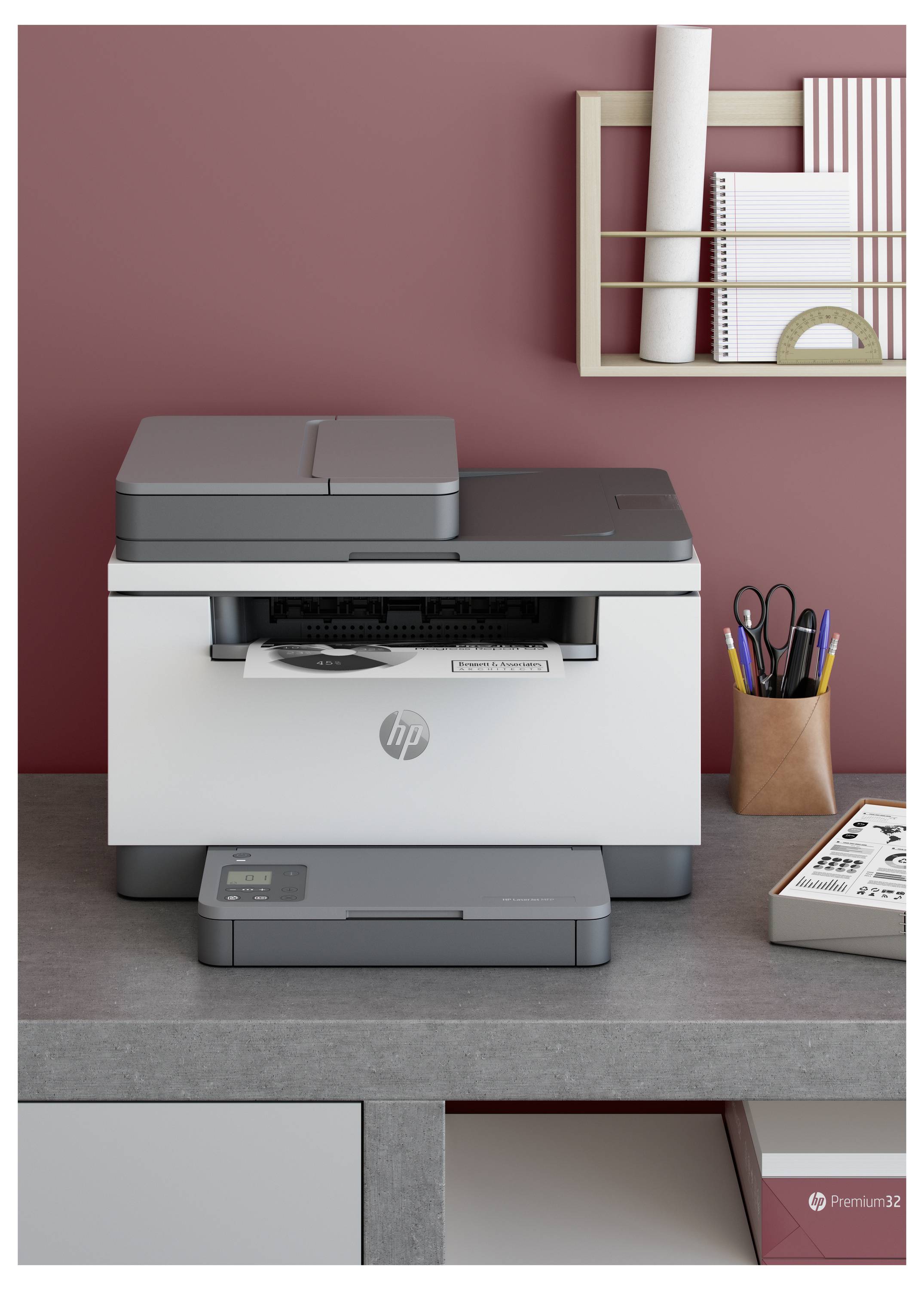 HP-Multifunktionsdrucker auf einem grauen Schreibtisch in einem Heimarbeitszimmer, mit Stiften und Notizbüchern auf dem Regal daneben.