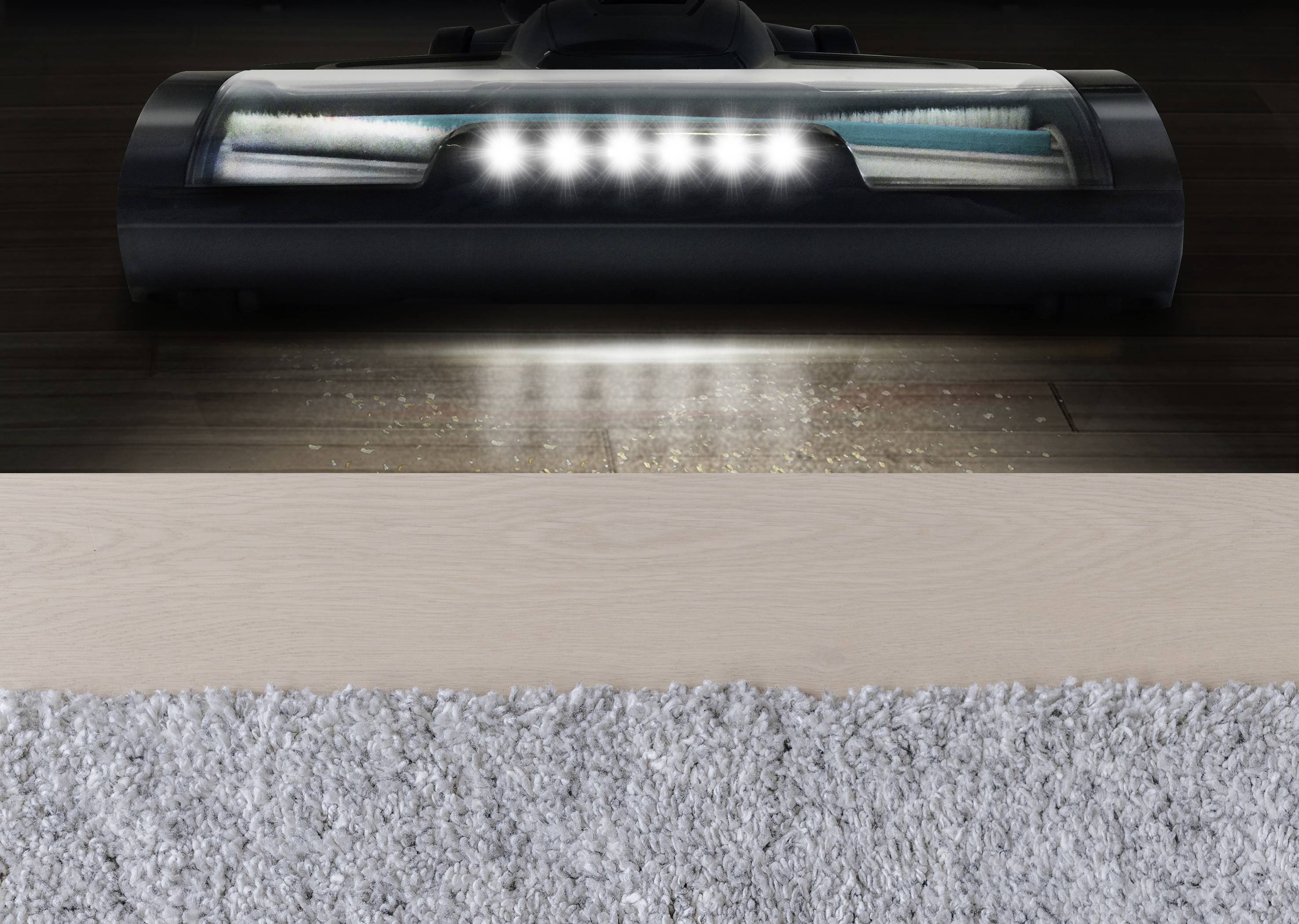 Ein Staubsauger mit LED-Lichtern saugt Staub von einem Holzfußboden neben einem Teppich.