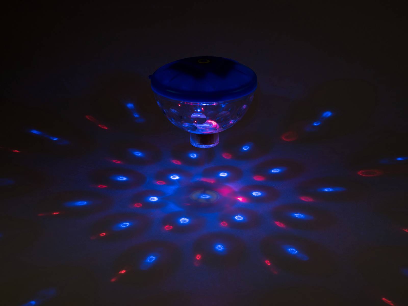 Eine leuchtende LED-Lampe projiziert ein Muster aus roten und blauen Lichtpunkten in einem dunklen Raum.
