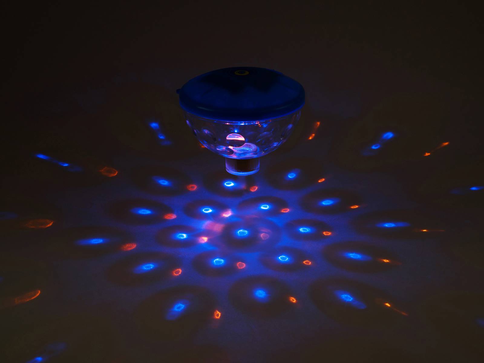 Ein Glaskörper dreht sich und projiziert bunte, blaue und rote Lichtmuster auf eine dunkle Oberfläche, die an ein Kaleidoskop erinnern.