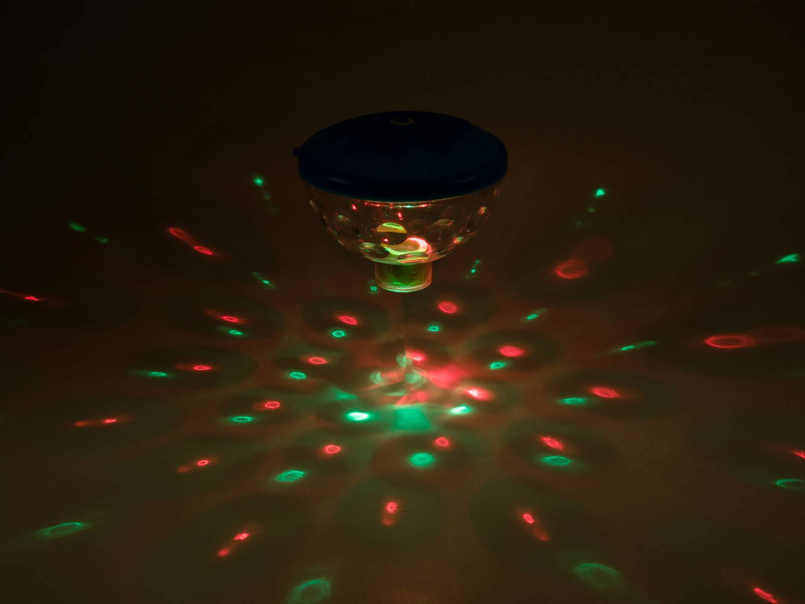 Ein beleuchtetes Kreiselspielzeug projiziert rote und grüne Lichteffekte in Kreisformen auf eine dunkle Oberfläche.
