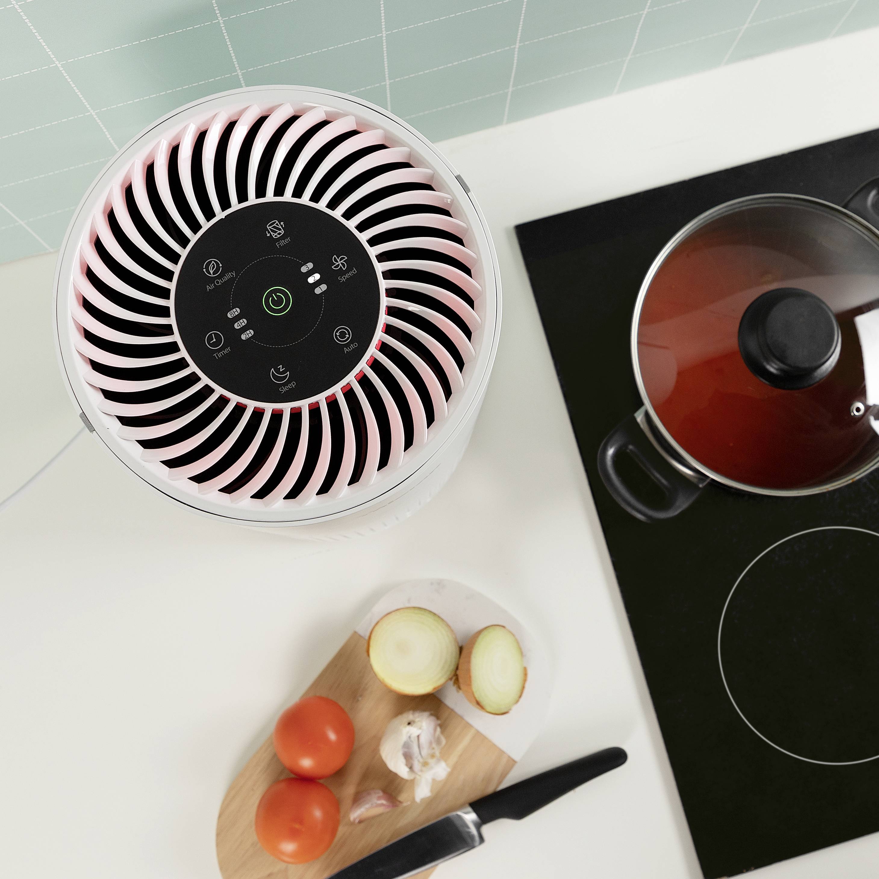 Ein Luftreiniger steht neben einem Herd mit Topf und einem Schneidebrett mit Tomaten, Zwiebel und Knoblauch auf einer Küchenarbeitsplatte.