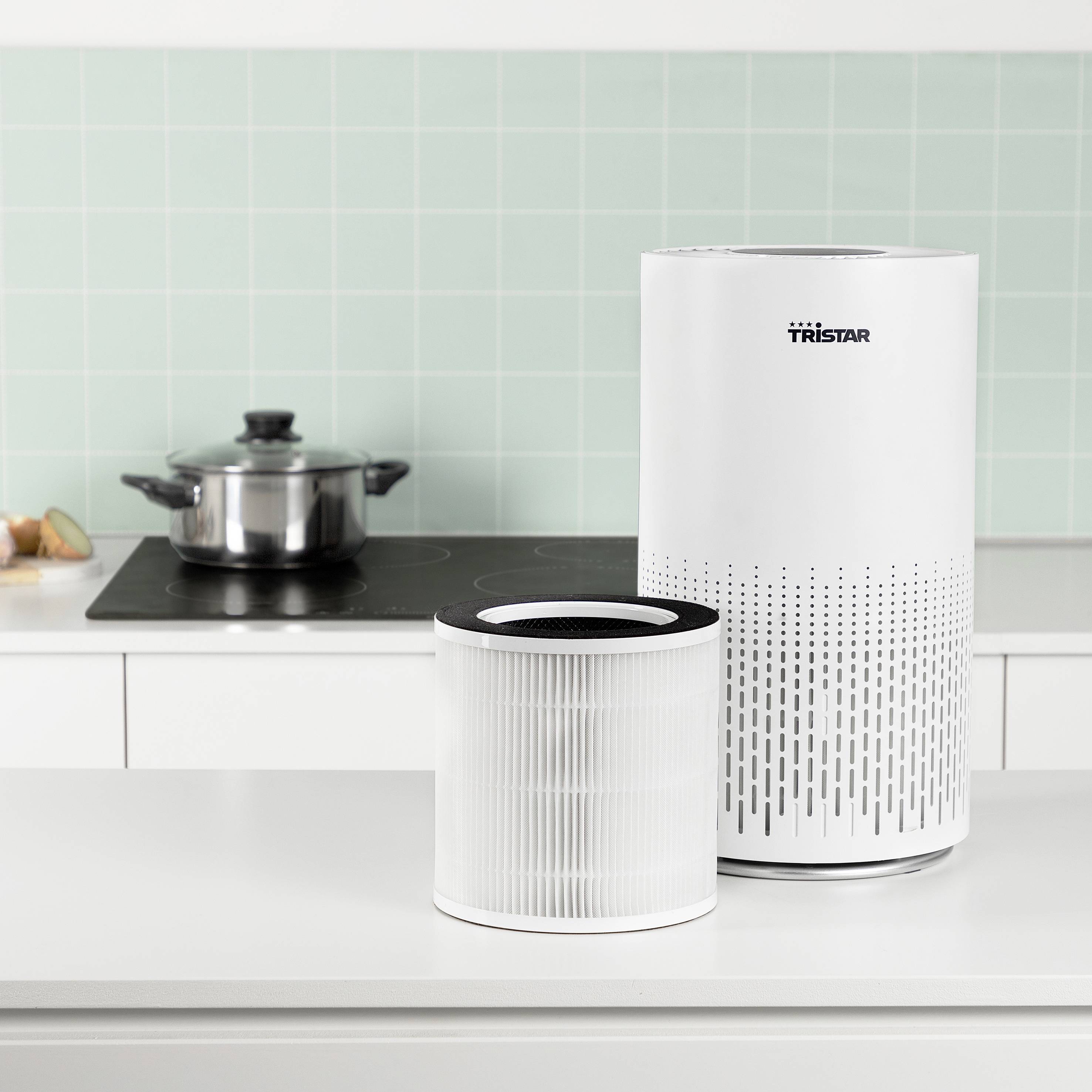 Luftreiniger und Filter auf einer Küchentheke mit einem Topf auf einem Herd im Hintergrund.