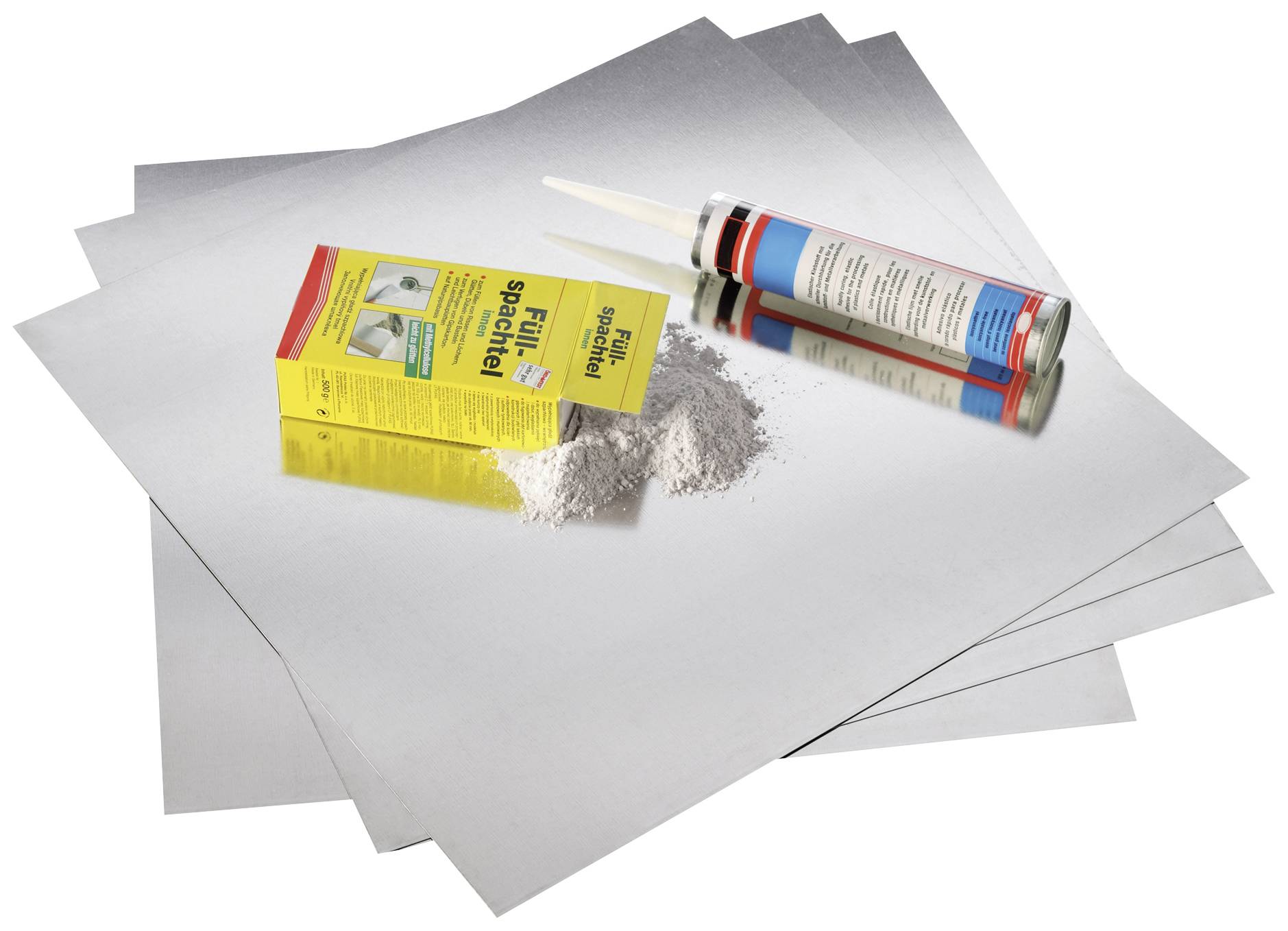 Eine Packung Reparaturspachtel und eine Kartusche Dichtmittel liegen auf mehreren grauen Metallplatten.