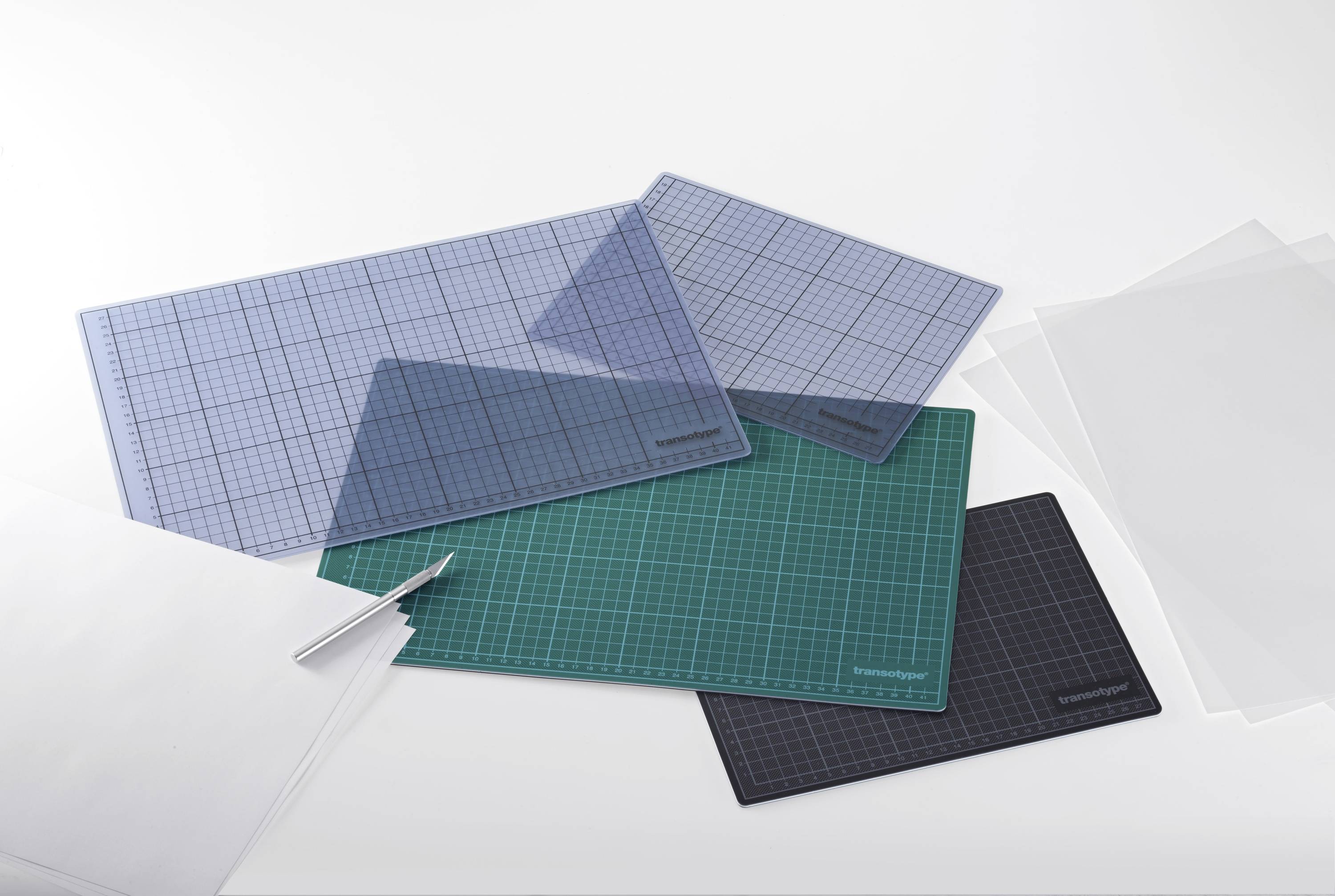 Mehrere Schneidematten in verschiedenen Farben und Größen liegen übereinander auf einem Tisch. Daneben liegt ein Schneidemesser.