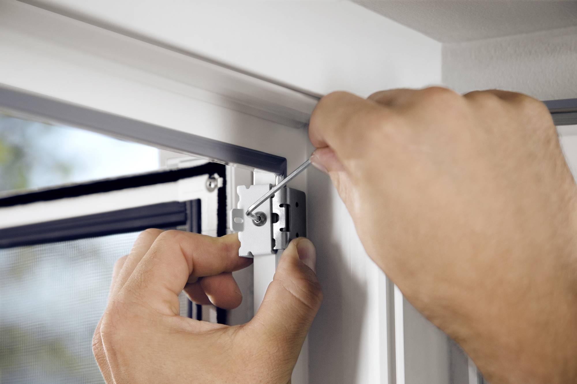 Eine Person justiert ein Scharnier an einem Fensterrahmen mit einem Schraubenzieher, möglicherweise zur Anpassung der Fensterfunktion.