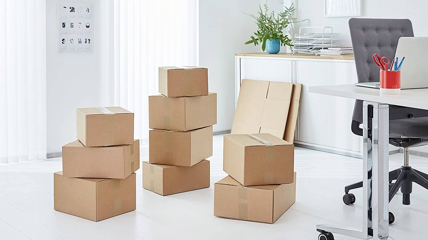 Kartonstapel in einem leeren Büro mit Schreibtisch und Pflanzen, Hinweis auf Umzug oder Renovierung.