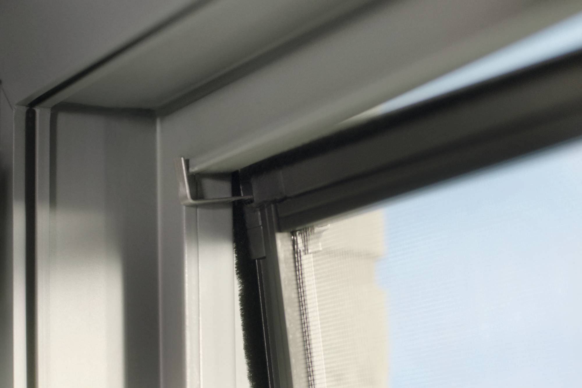 Ein Fenster mit einem eingebauten Insektenschutzgitter, das teilweise geöffnet ist, zeigt einen klaren Himmel im Hintergrund.