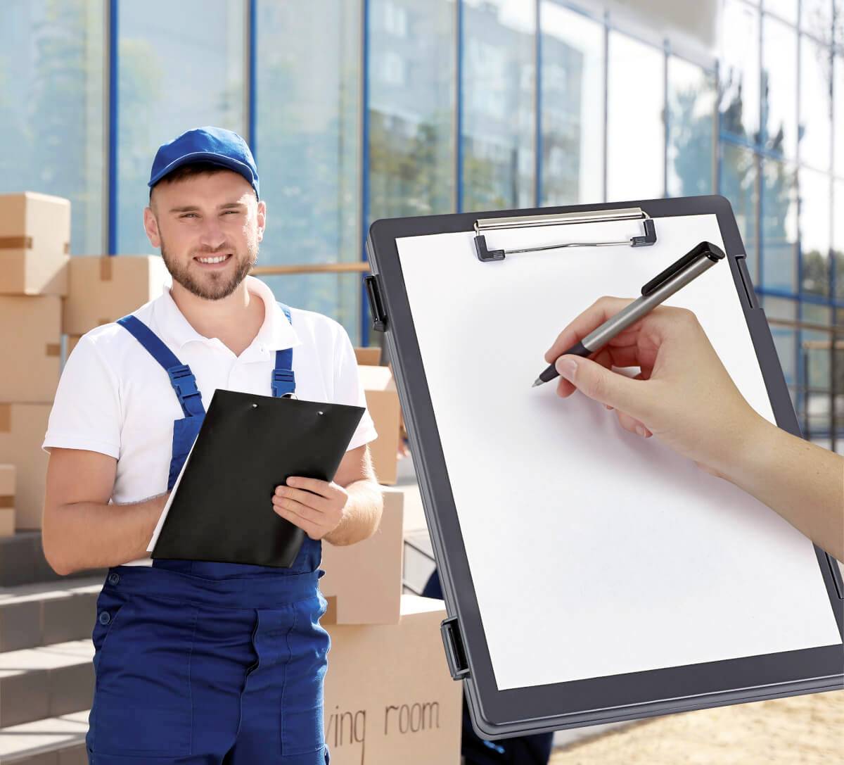 Ein Mann in blauer Arbeitskleidung und Mütze steht mit einem Klemmbrett vor Kartons; eine Hand schreibt auf ein Papier.