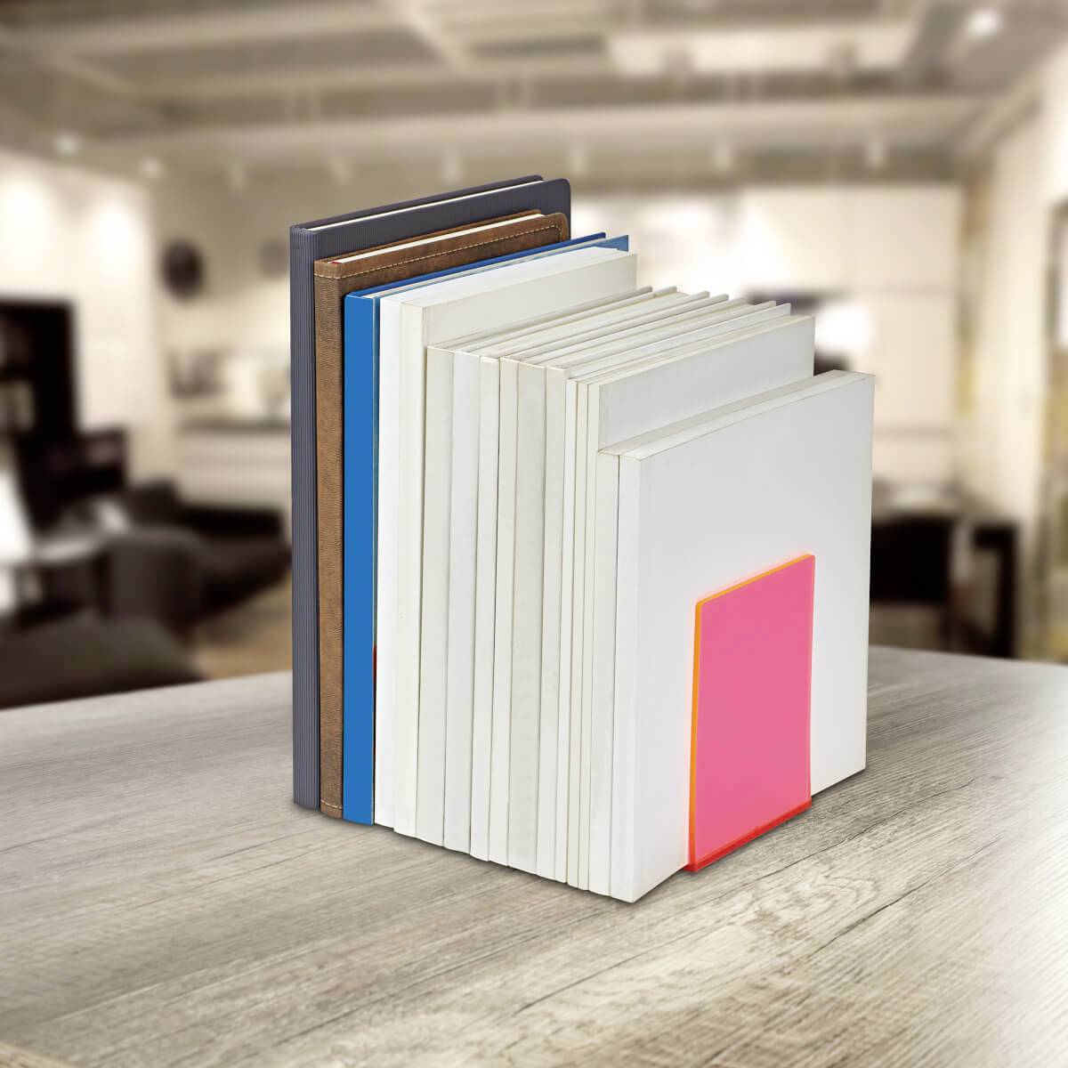 Bücher stehen aufrecht auf einem Tisch, gestützt von einem pinkfarbenen Buchstütze. Der Hintergrund zeigt einen unscharfen Innenraum.