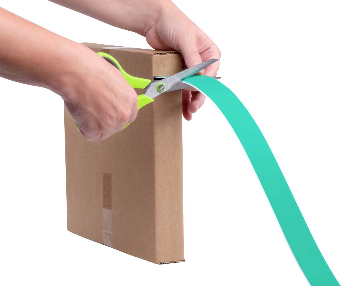 Person schneidet mit einer grünen Schere ein türkisfarbenes Band an einem braunen Karton ab.
