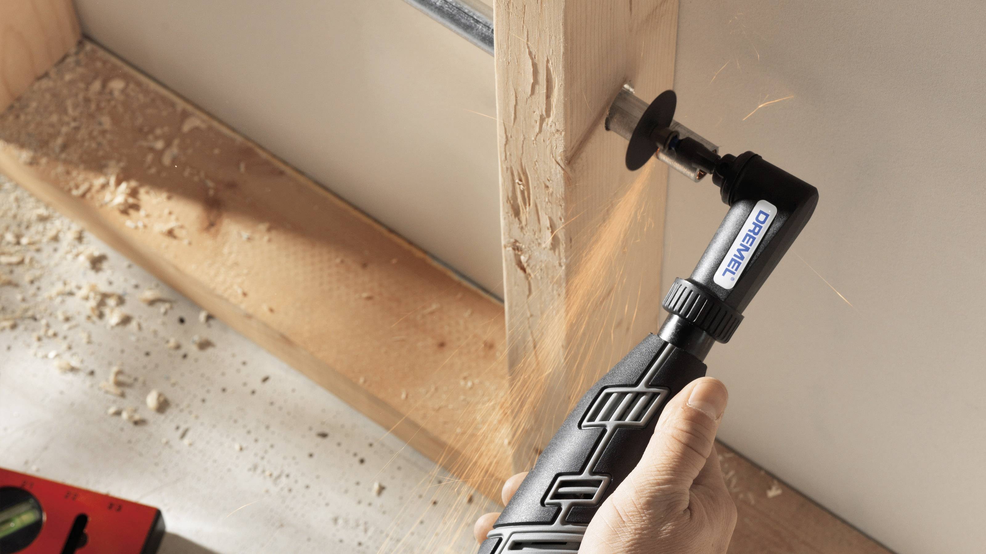 Eine Hand hält ein elektrisches Multifunktionswerkzeug, das Holz bearbeitet. Funken sprühen beim Schneiden durch einen dicken Holzbalken.