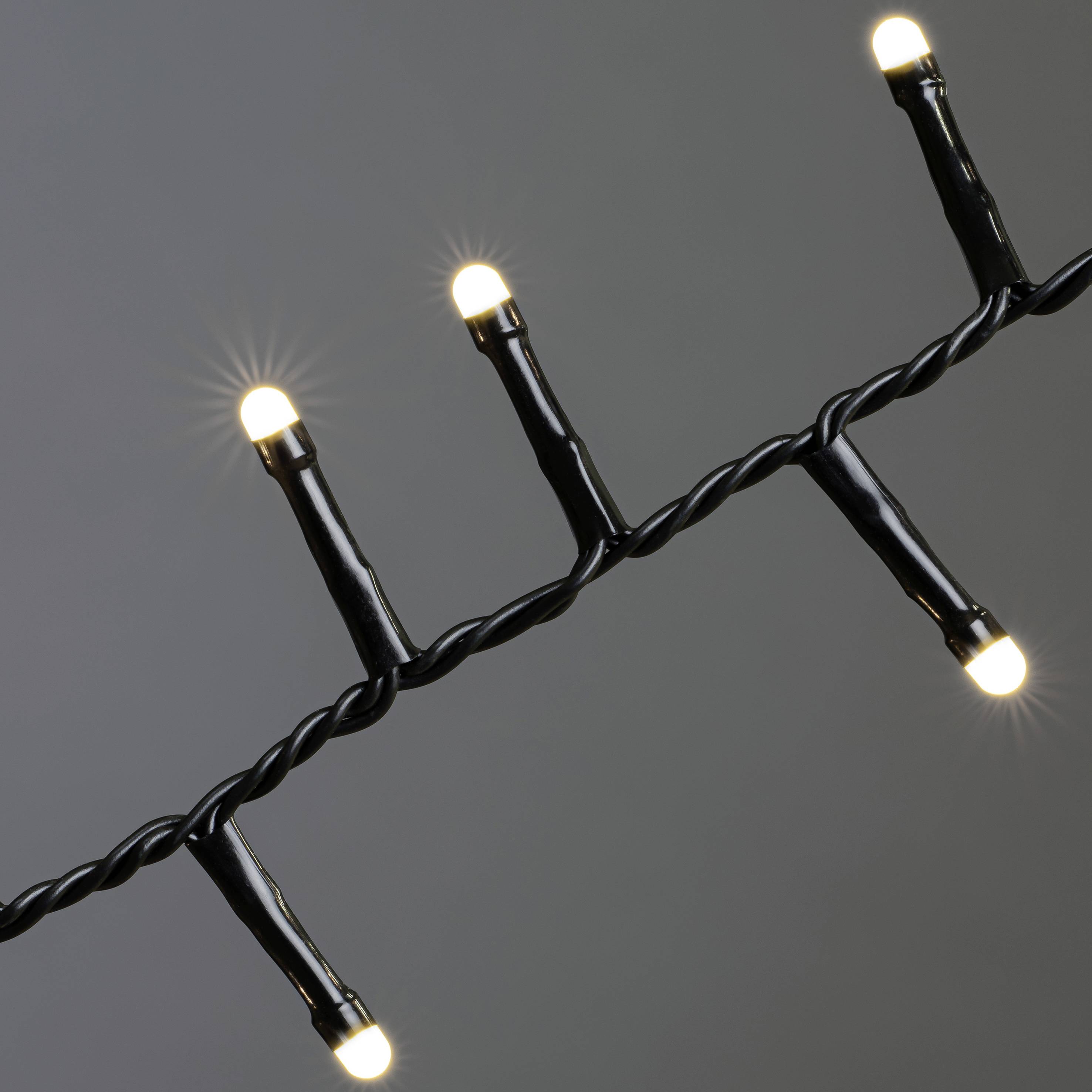 Eine Lichterkette mit mehreren leuchtenden weißen Glühbirnen, gleichmäßig verteilt auf schwarzem Kabel, vor grauem Hintergrund.