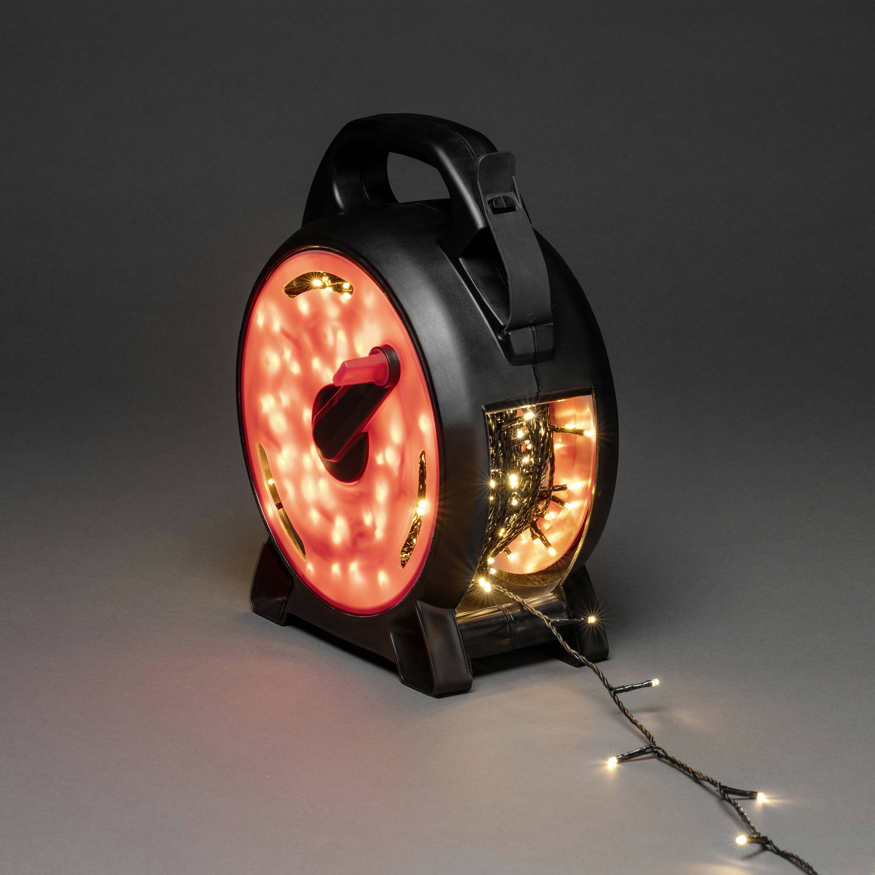 Schwarze Kabeltrommel mit Weihnachtsbeleuchtung, die aufgerollt ist, das Licht sanft leuchtet und eine festliche Stimmung erzeugt.