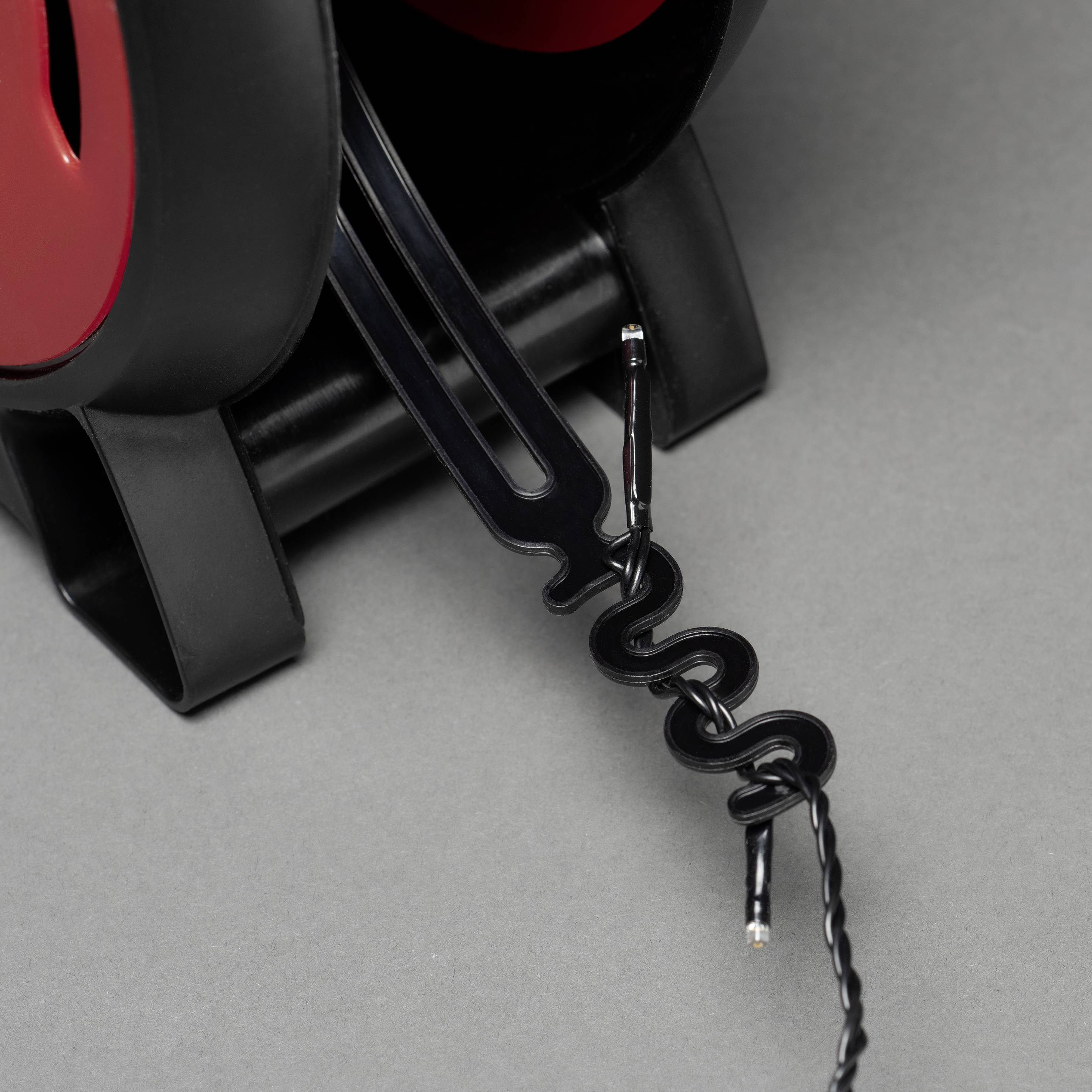 Ein schwarzer Kabelhalter mit einem eingesteckten roten Kabel, das spiralförmig gewickelt ist. Der Halter steht auf einer grauen Fläche.