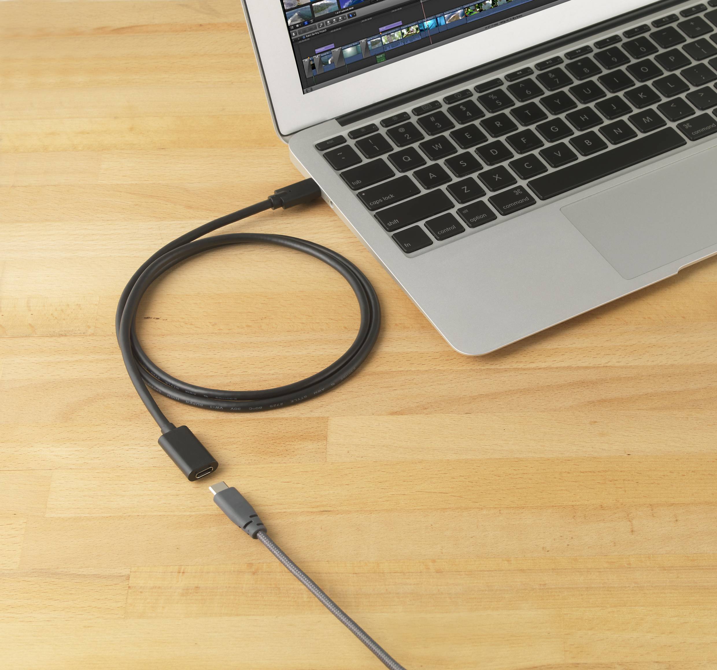 Ein Laptop auf einem Holztisch mit einer Bildbearbeitungssoftware auf dem Bildschirm. Ein USB-C-Kabel liegt daneben.