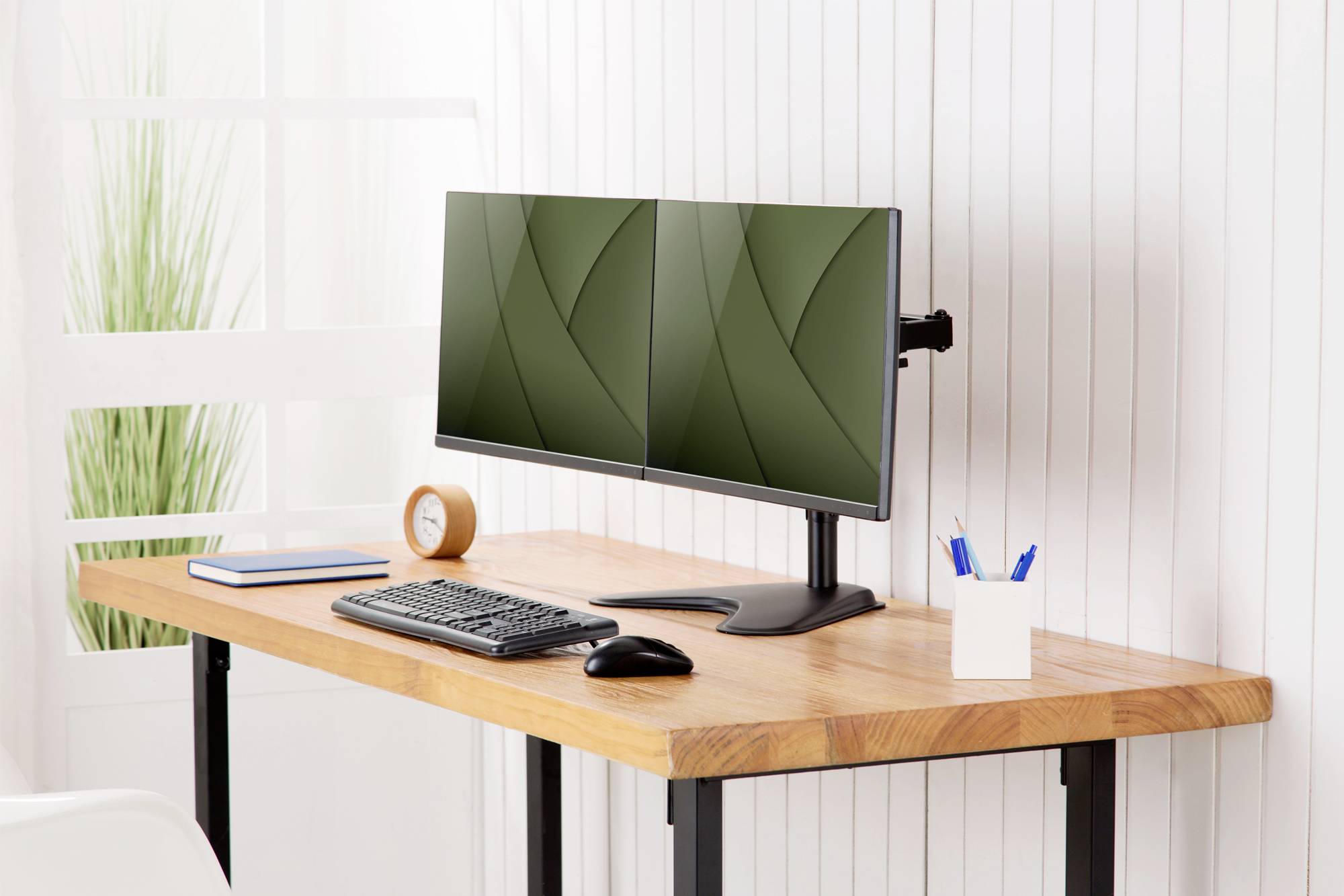 Ein minimalistischer Schreibtisch mit einem Doppelmonitor-Setup, einer Tastatur, einer Maus, einem Stiftbehälter und einem Buch.