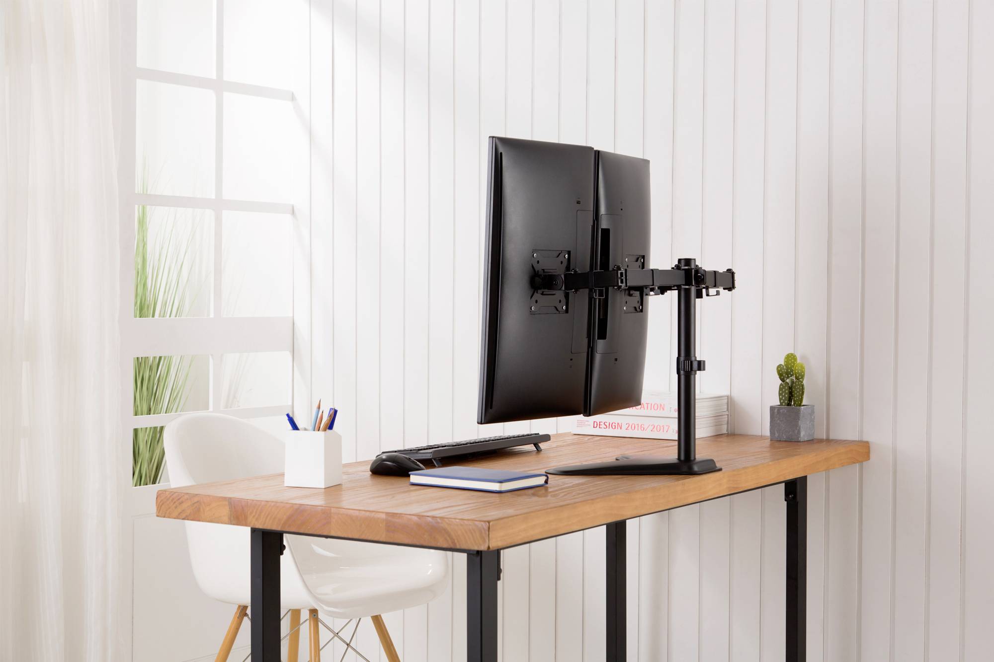 Ein Monitor ist auf einem Schreibtisch mit Holzoberfläche in einem hellen Raum angebracht. Daneben stehen eine Tasse und Stifte.