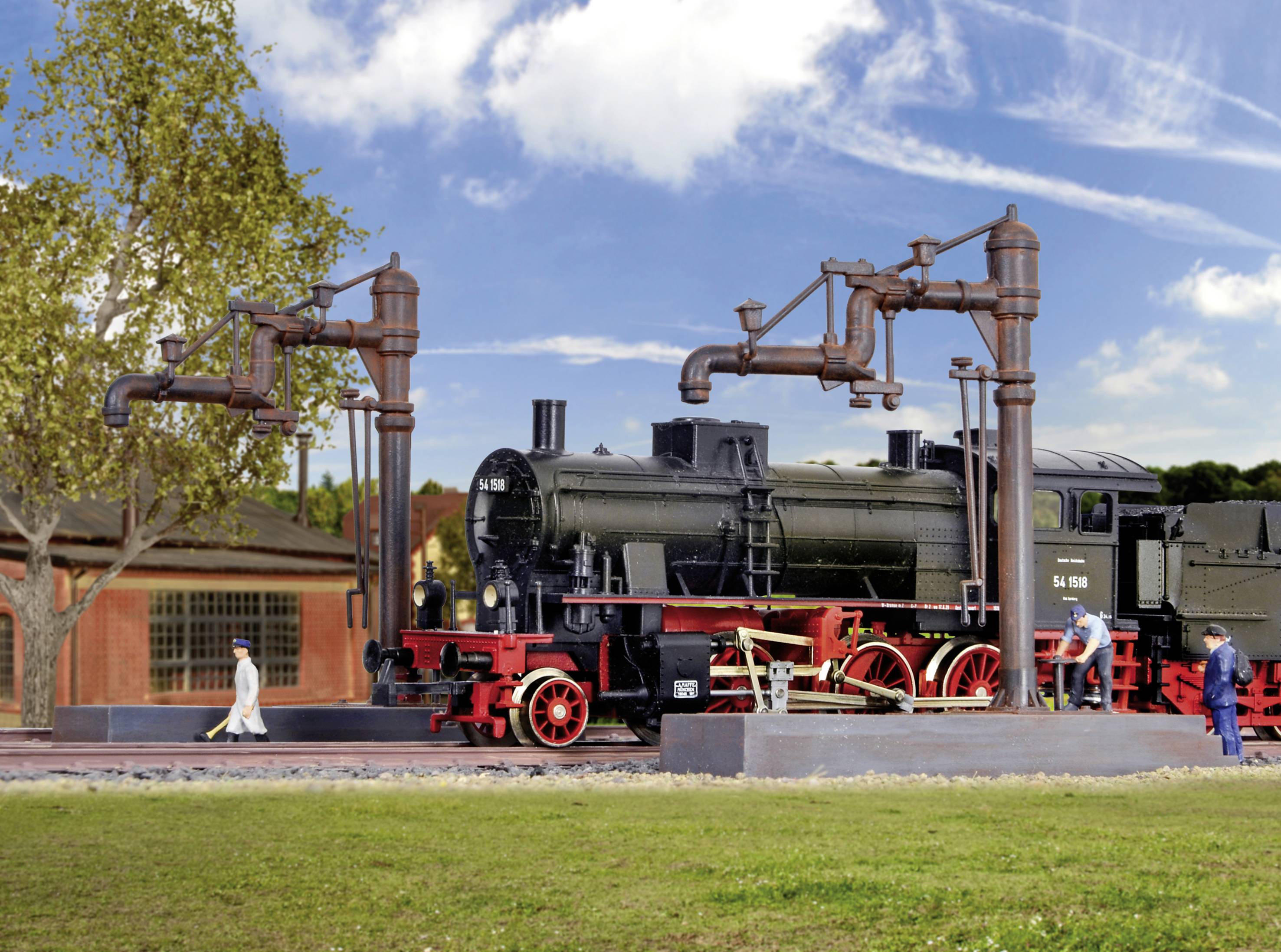 Eine schwarze Dampflokomotive steht auf einem Bahnhofsgleis. Zwei Arbeiter sind mit Wartungsarbeiten beschäftigt, Bäume im Hintergrund.