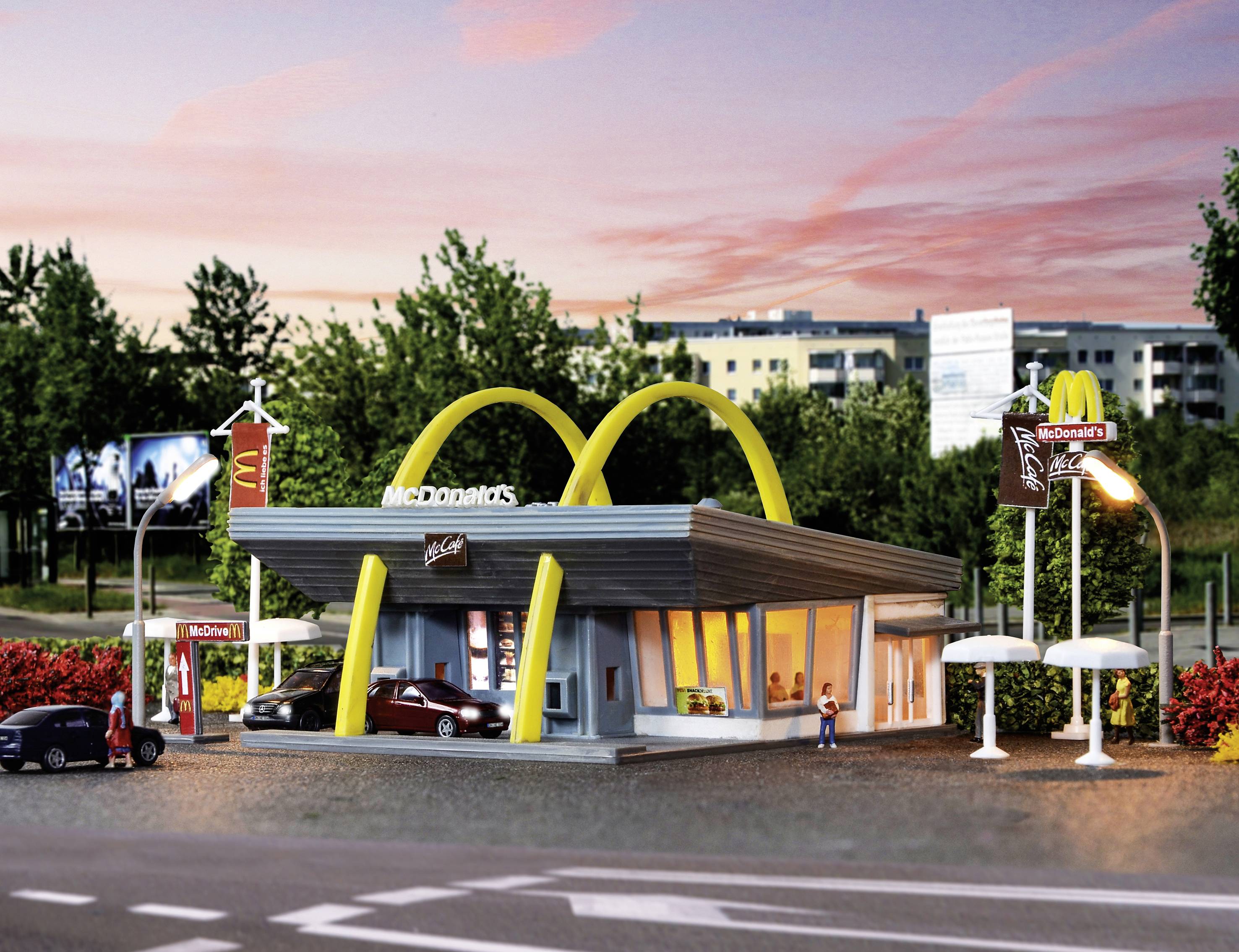 Ein Miniaturmodell eines McDonald's-Restaurants mit auffälligen gelben Bögen, Autos davor. Hintergrund zeigt Bäume und Gebäude.