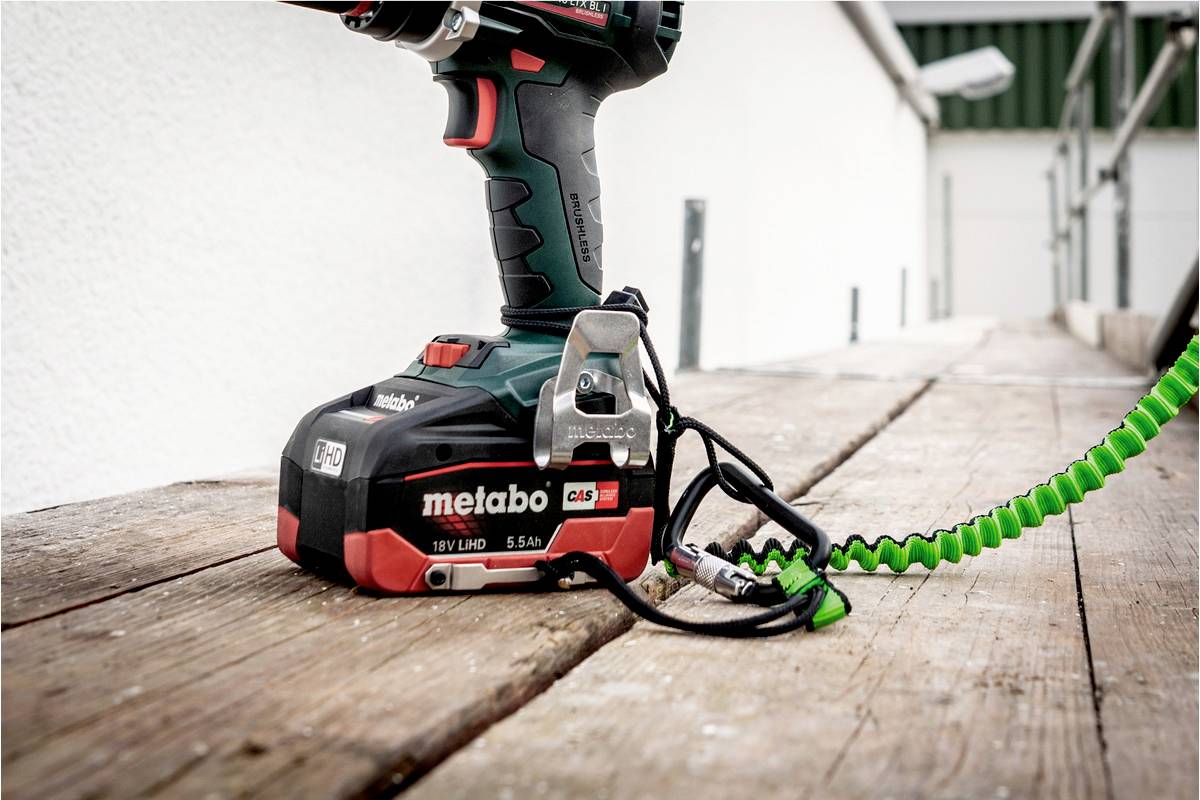 Ein Akkuschrauber der Marke Metabo mit grüner Spiralschnur liegt auf einem Holzbrett im Freien.