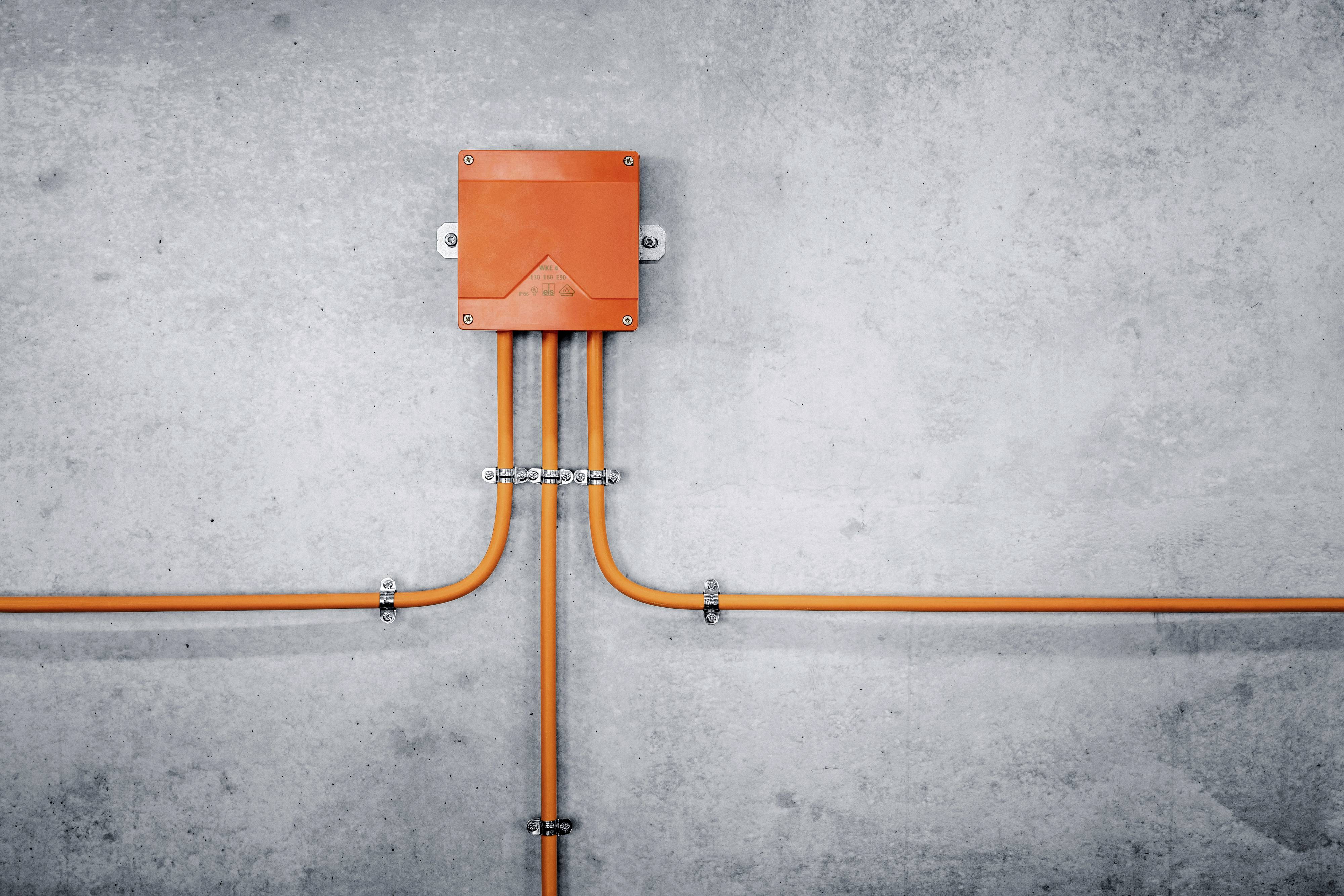 Orange Kabelbox an grauer Betonwand mit abgehenden Kabeln links und rechts.