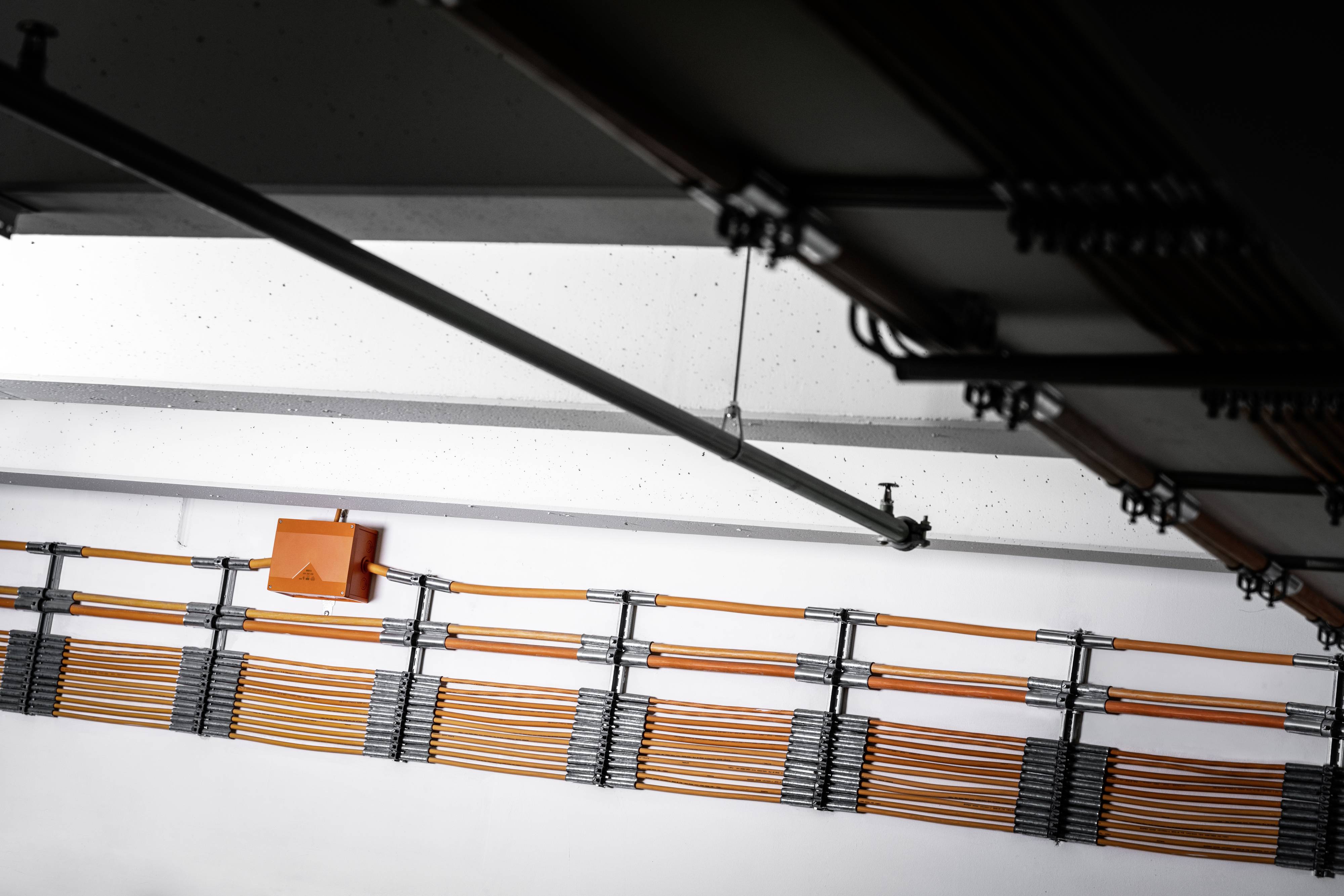 Orangefarbene Kabelkanäle verlaufen parallel zur Decke eines Gebäudes. Ein orangefarbener Kasten ist an der Wand befestigt.
