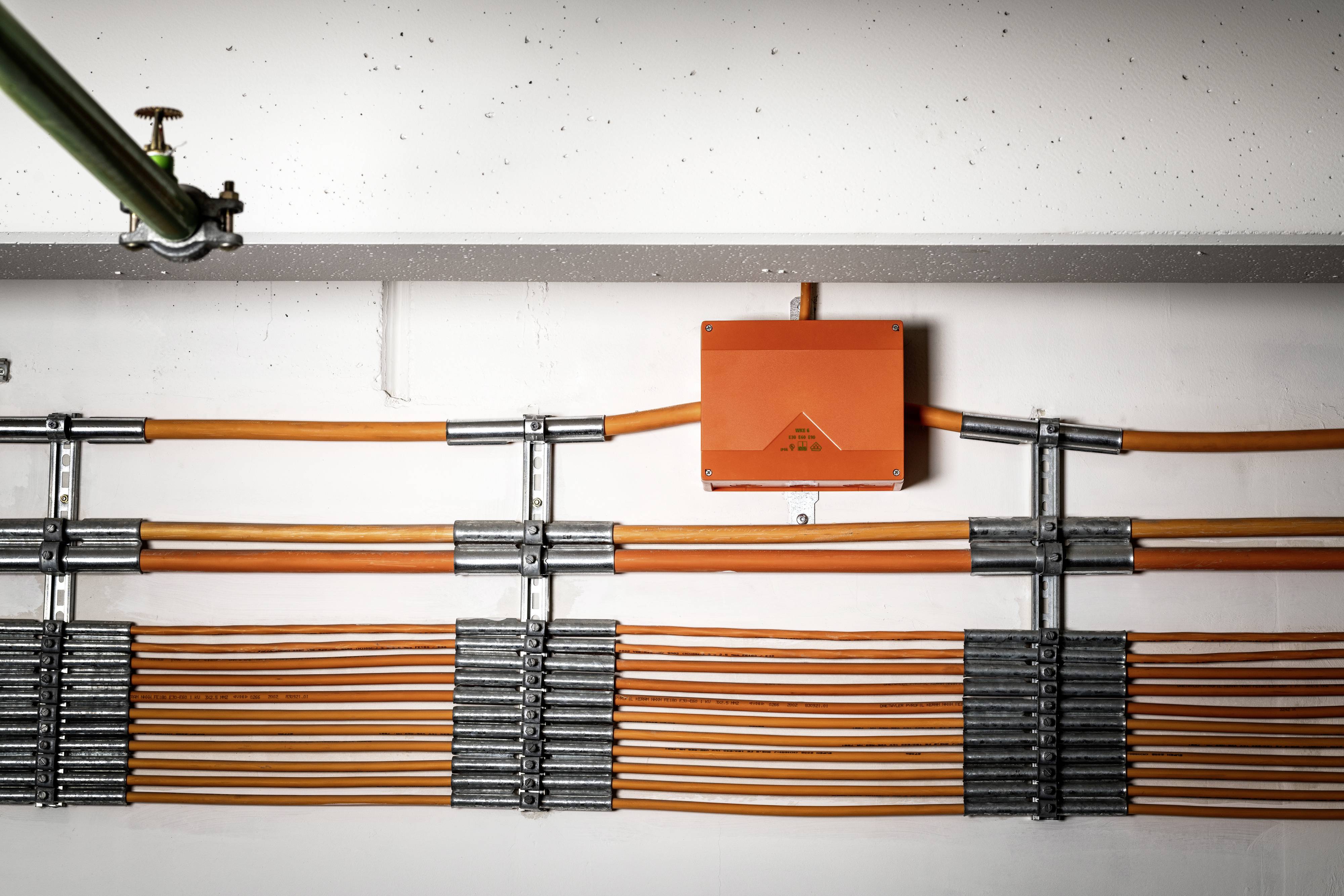 Orange Kabel in Metallklemmen an der weißen Decke befestigt. Eine orange Box in der Mitte verbindet die Kabel.